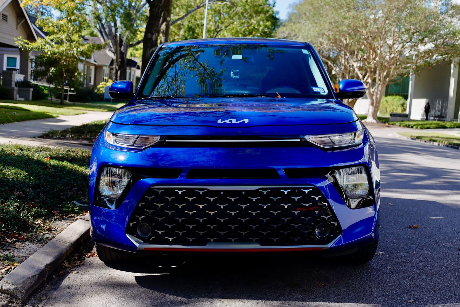 Front view of a bright blue Kia Soul compact SUV parked on a suburban street with trees in the background.