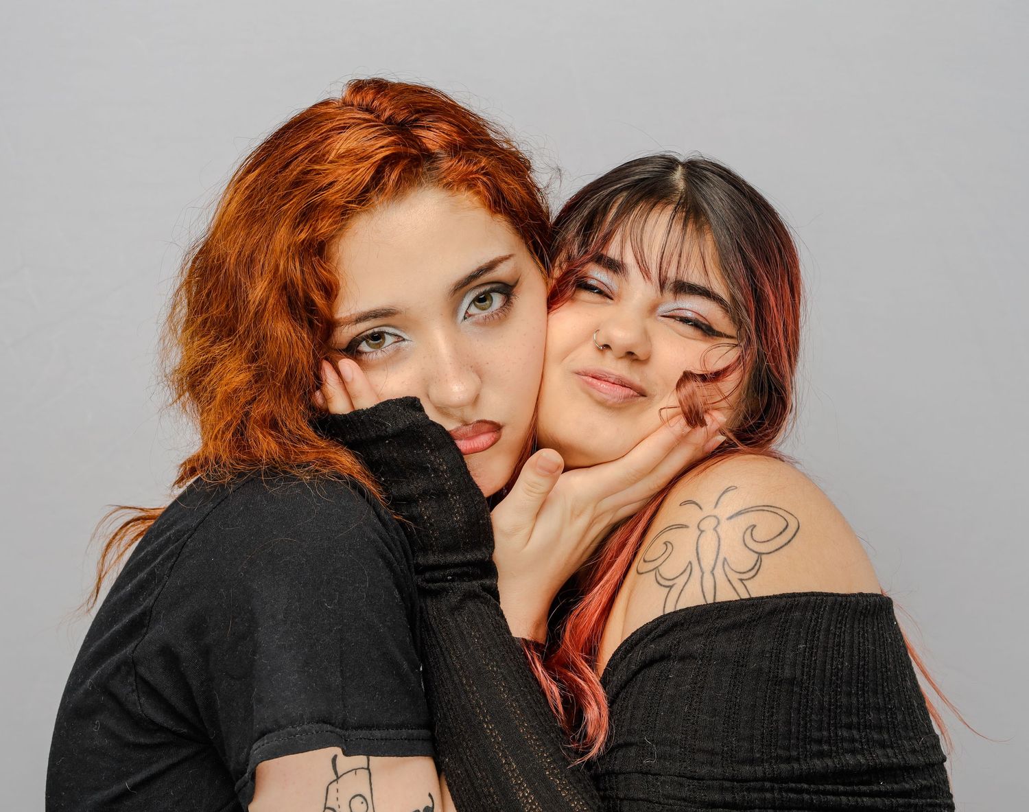 Two tattooed friends in black clothing making playful expressions together in studio photo.