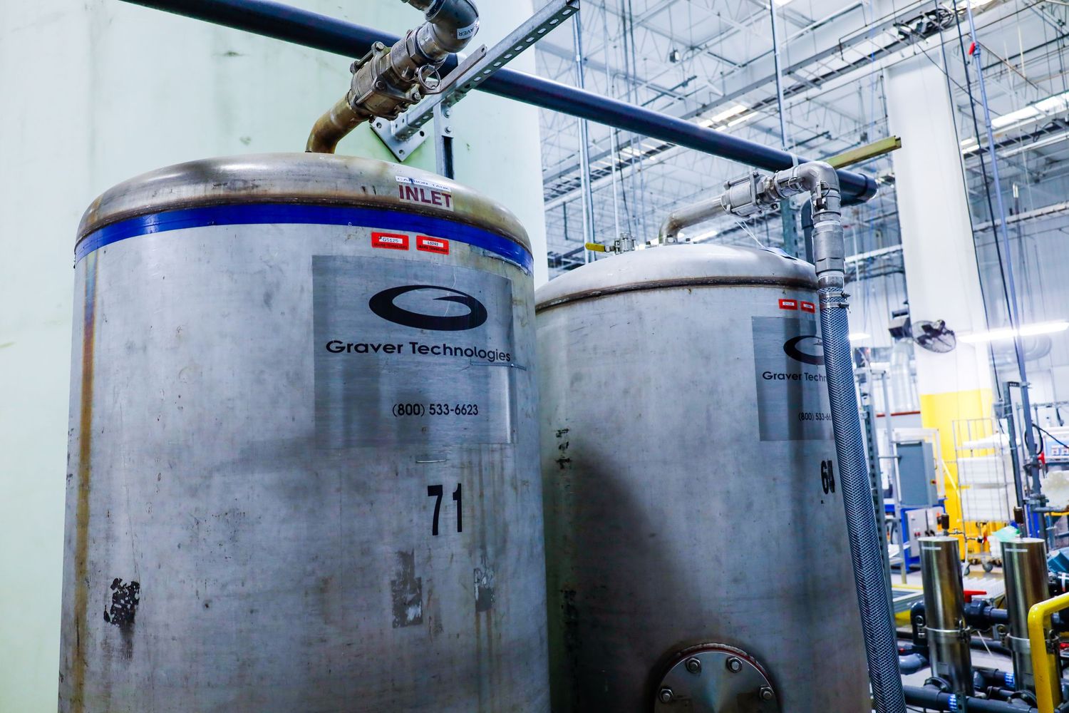Large industrial stainless steel brewing tanks with pressure gauges and piping in a manufacturing facility.