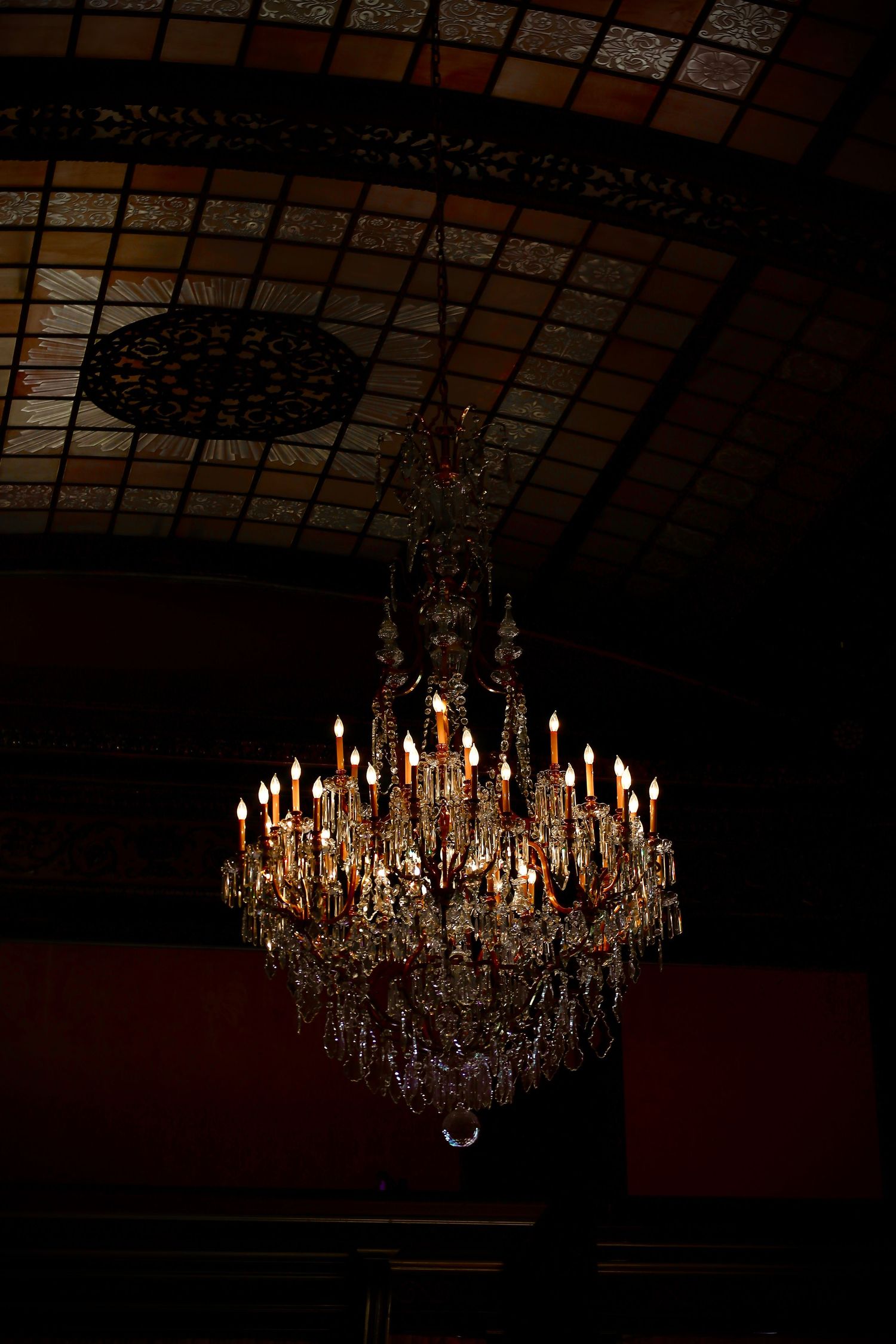 Ornate vintage crystal chandelier with multiple tiers of candle lights against a dark ceiling.
