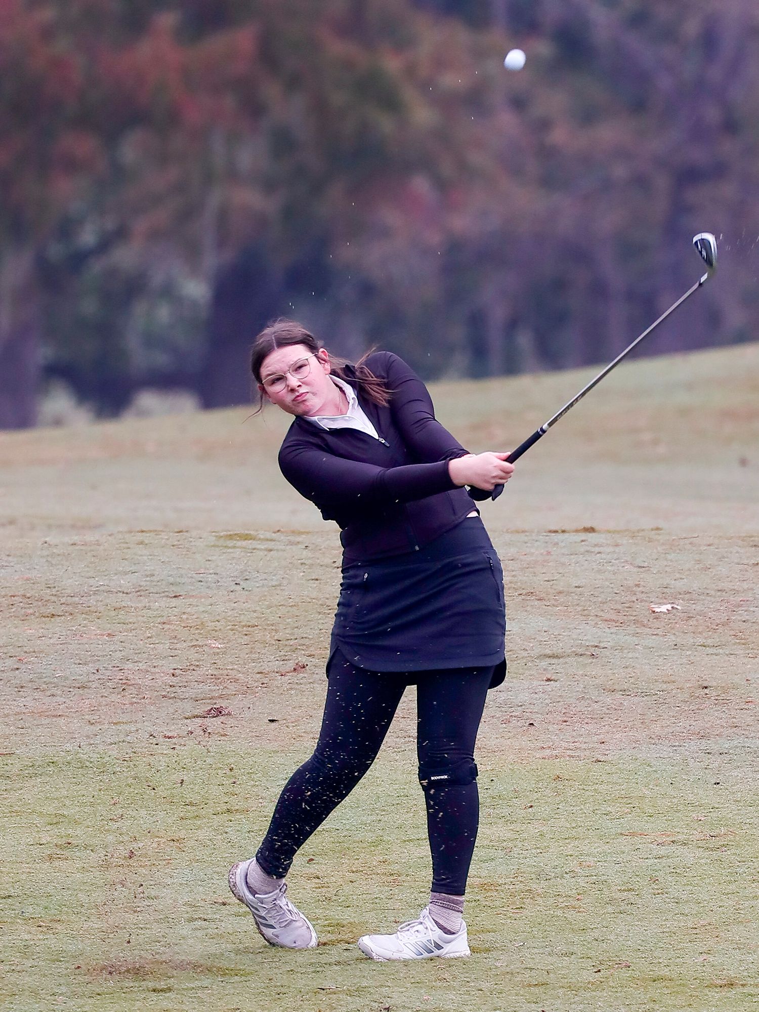 Golfer in dark attire follows through on swing during practice on autumn golf course with vibrant fall foliage backdrop.