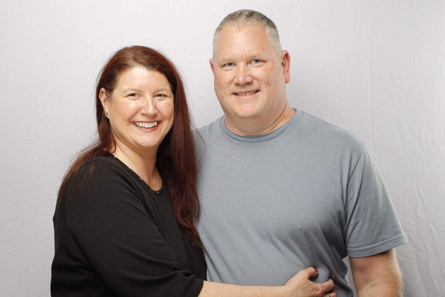 A couple wearing black and gray tops smiling warmly against a light background.