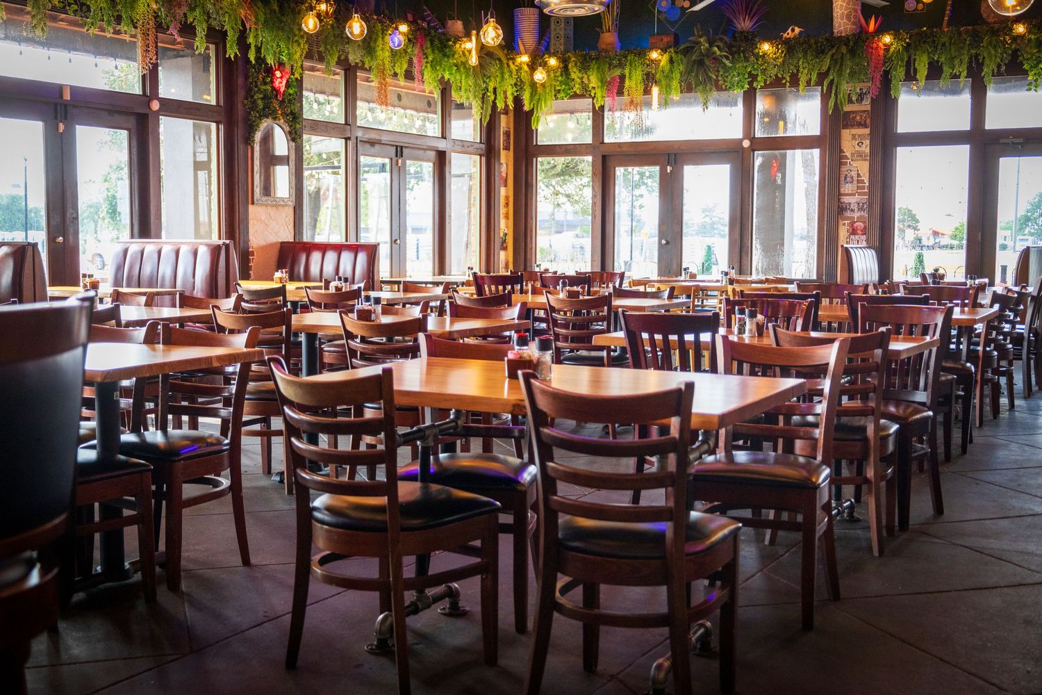 Empty restaurant dining room with wooden chairs and tables decorated with festive garlands and string lights.