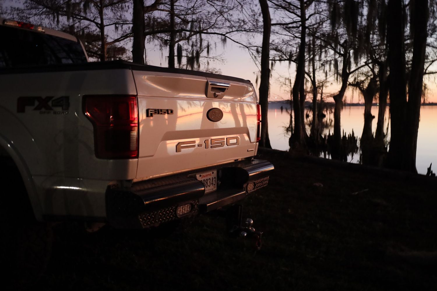 Ford F150 pickup truck parked along waterfront during golden sunset with cypress trees.