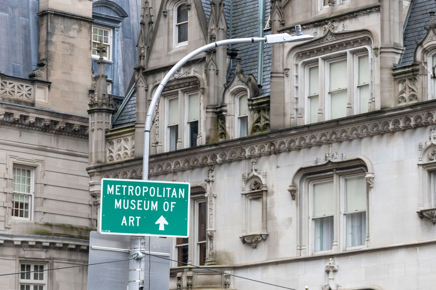 A green directional street sign for the Metropolitan Museum of Art against the backdrop of ornate stone architecture.