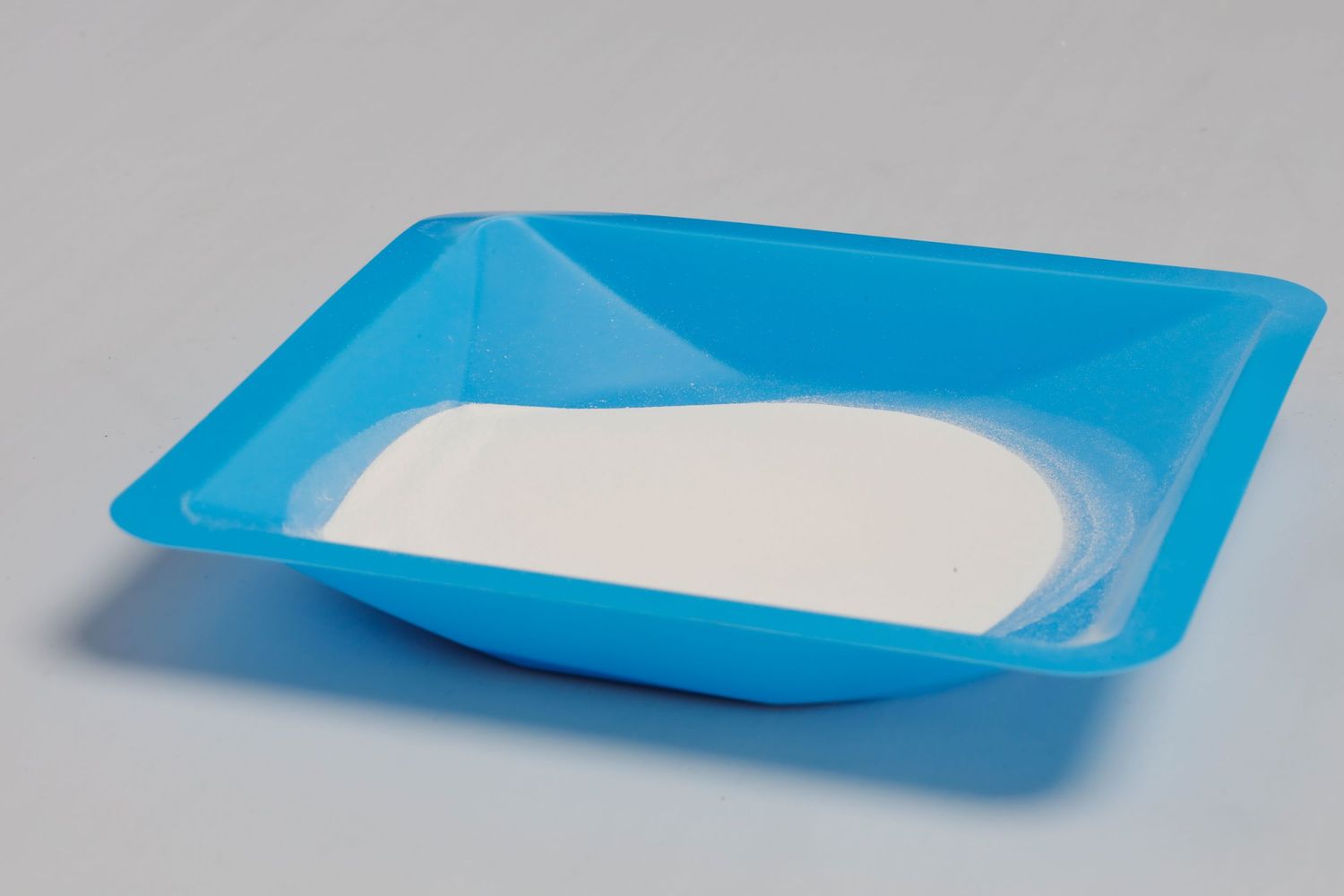 A light blue plastic medical tray containing white powder on a gray background.