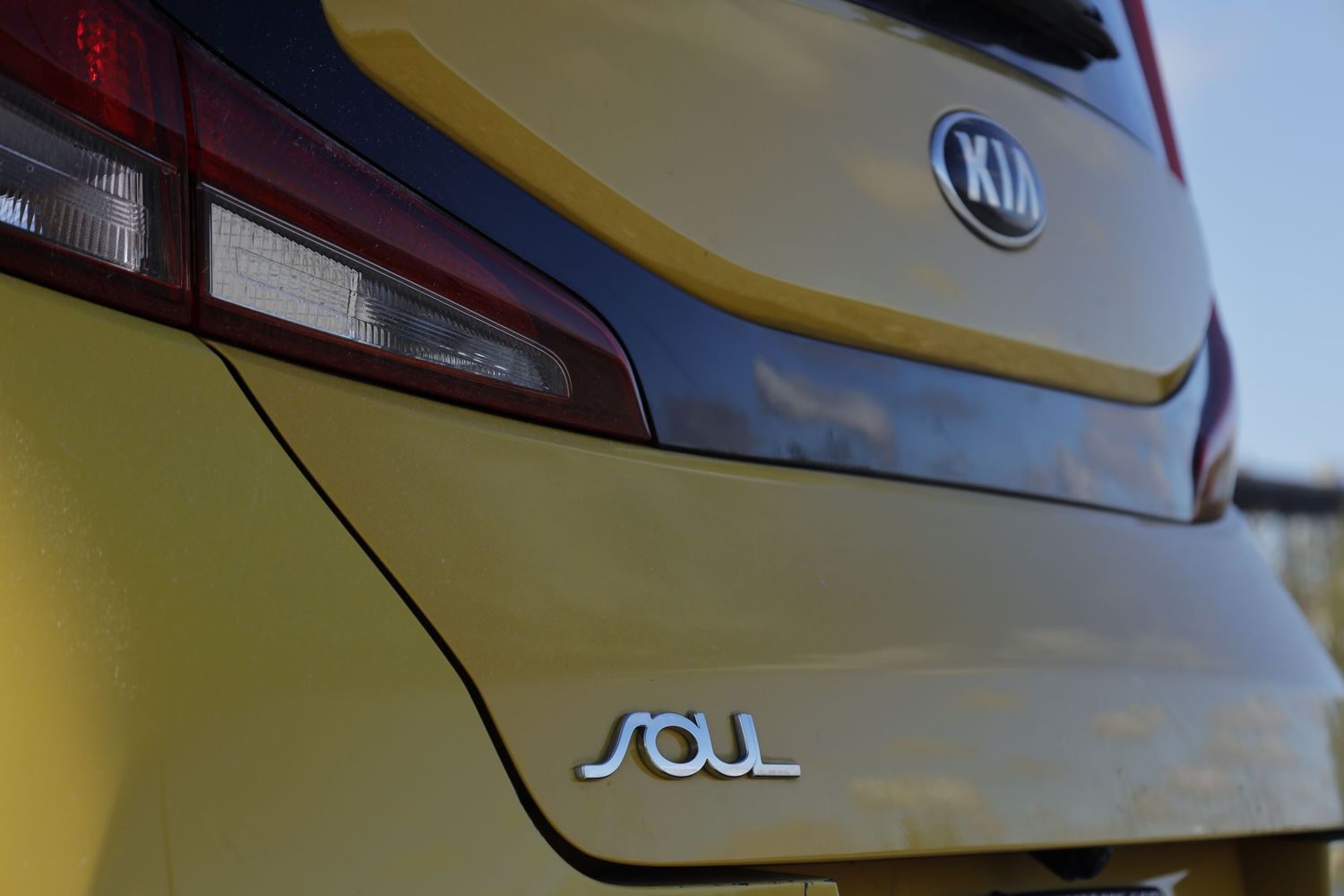 Close-up shot of a yellow Kia Soul vehicle's rear end showing the Soul badge and taillight detail against a blurred background.