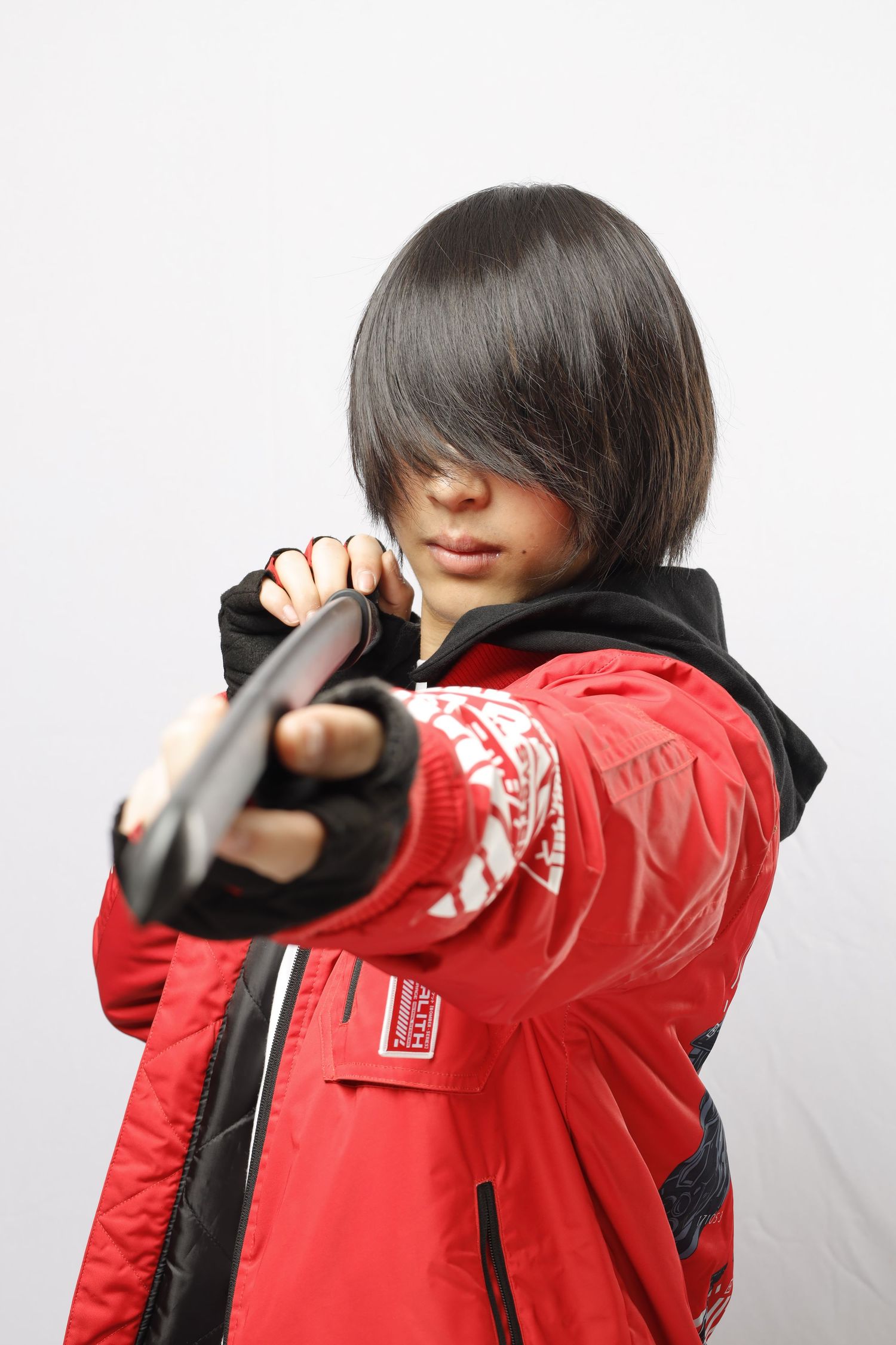 Person in red winter jacket and black hoodie poses with hair covering face while holding out their arm.