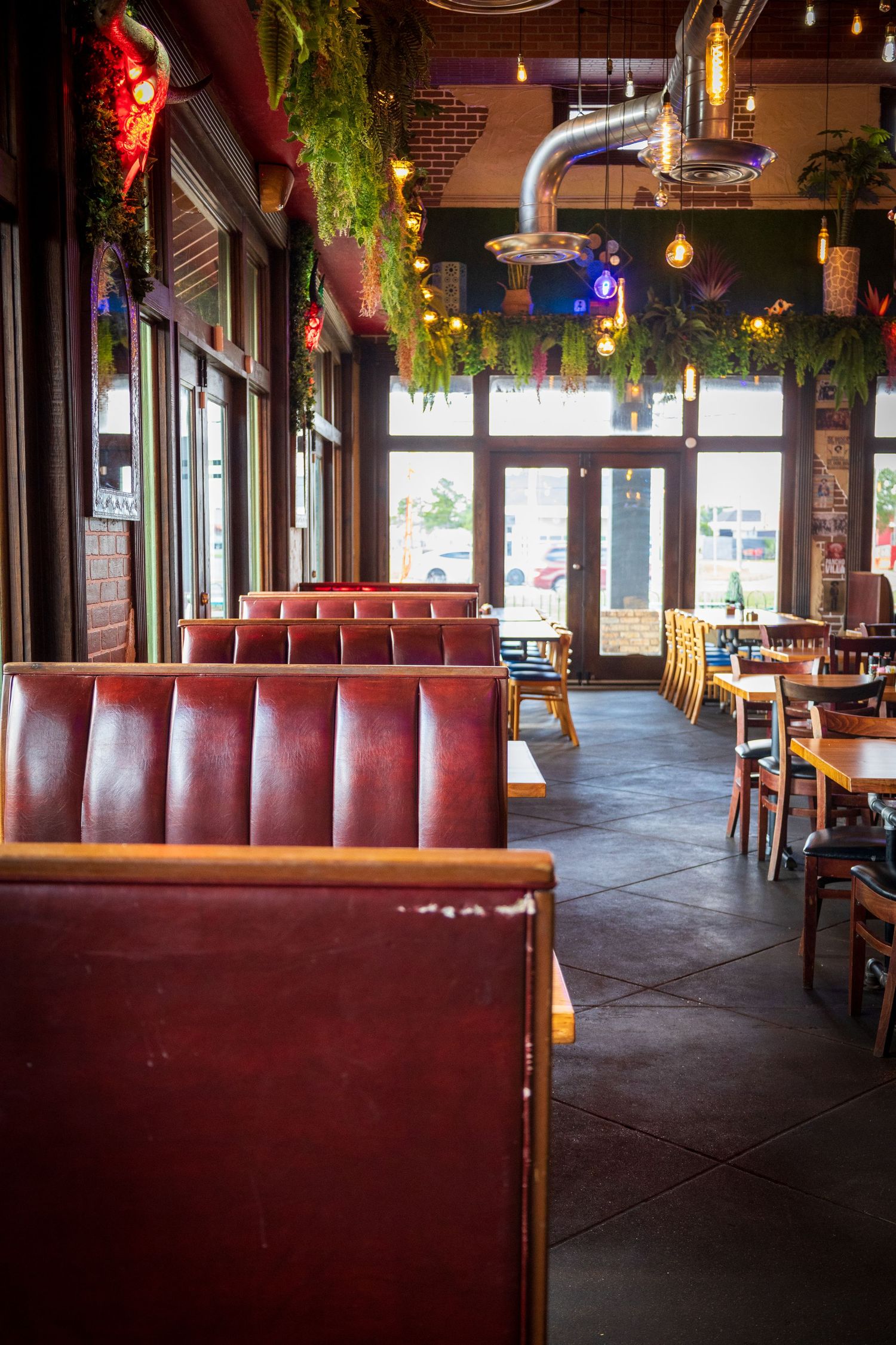 Restaurant interior with red leather booths and hanging plants under warm lighting.