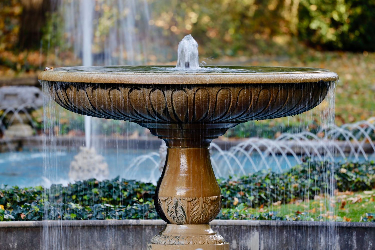 Classical stone fountain with water features and a decorative bird statue in a garden setting.