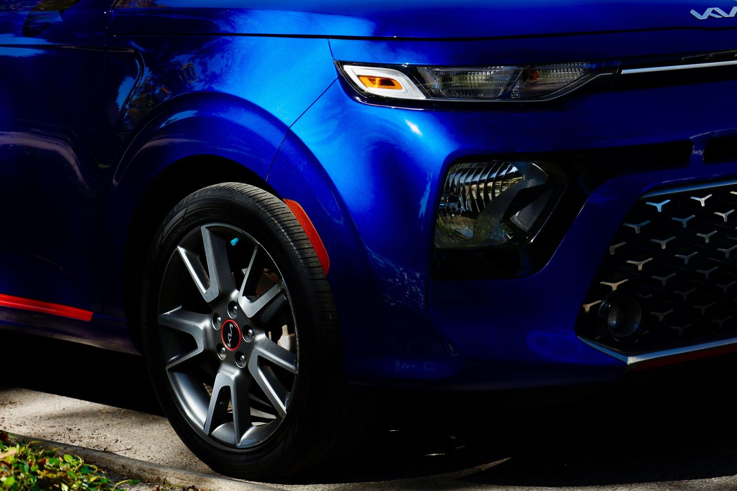Close-up of a blue Kia Soul's front headlight and wheel detail in dramatic lighting.