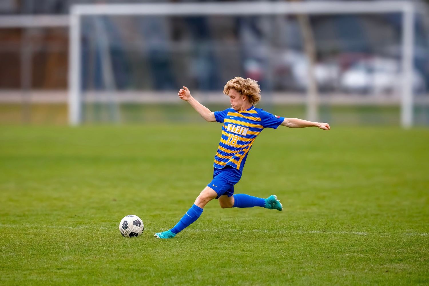 Young soccer player in blue and white striped jersey prepares to kick ball on grassy field.