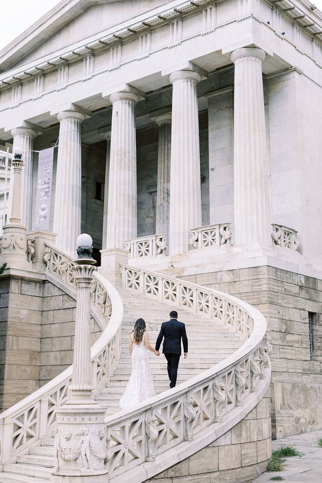 bride and groom walking up the stairs of a neoclassical building in Athens holding hands