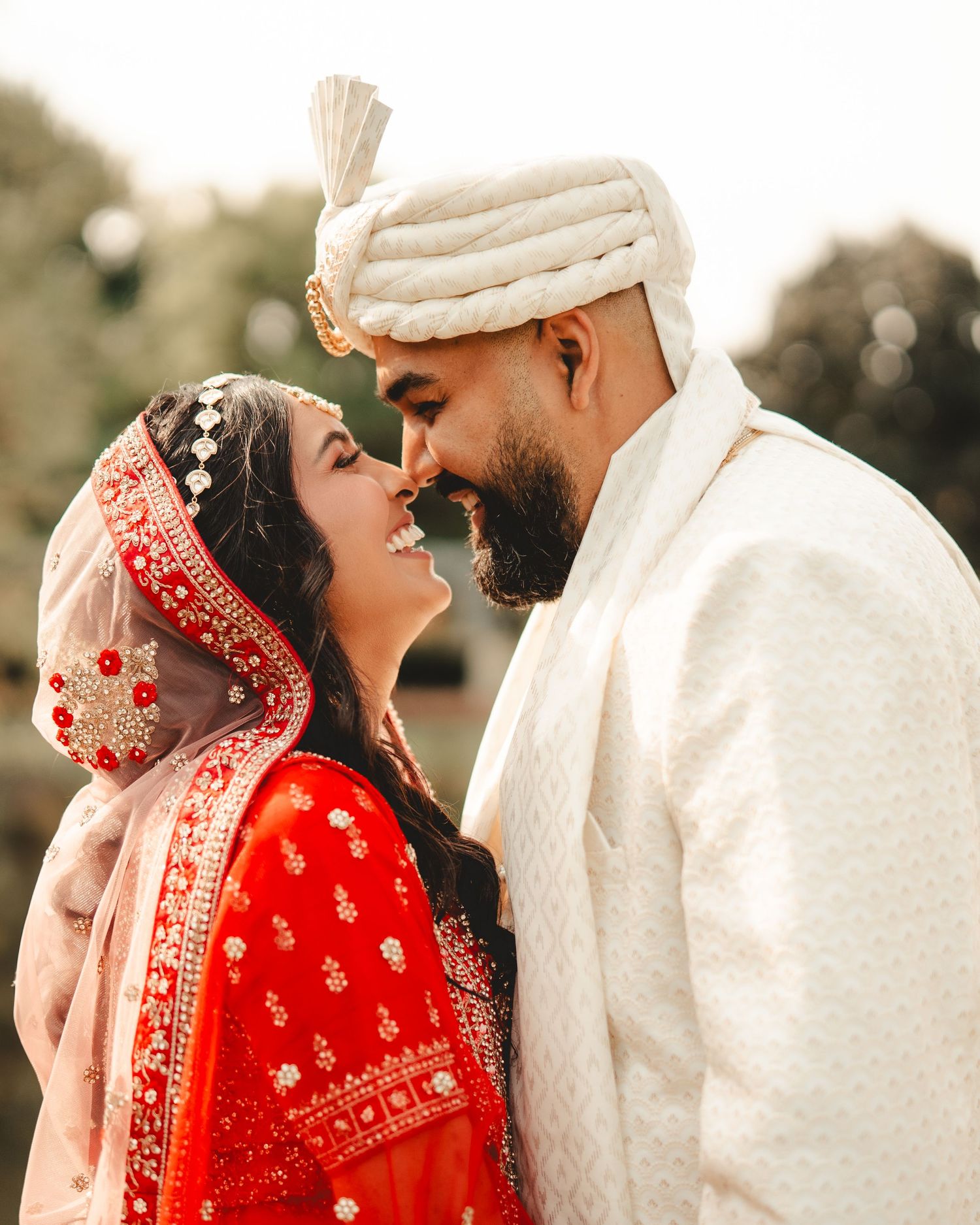 A couple in Indian wedding attire shares a romantic moment against a natural backdrop.