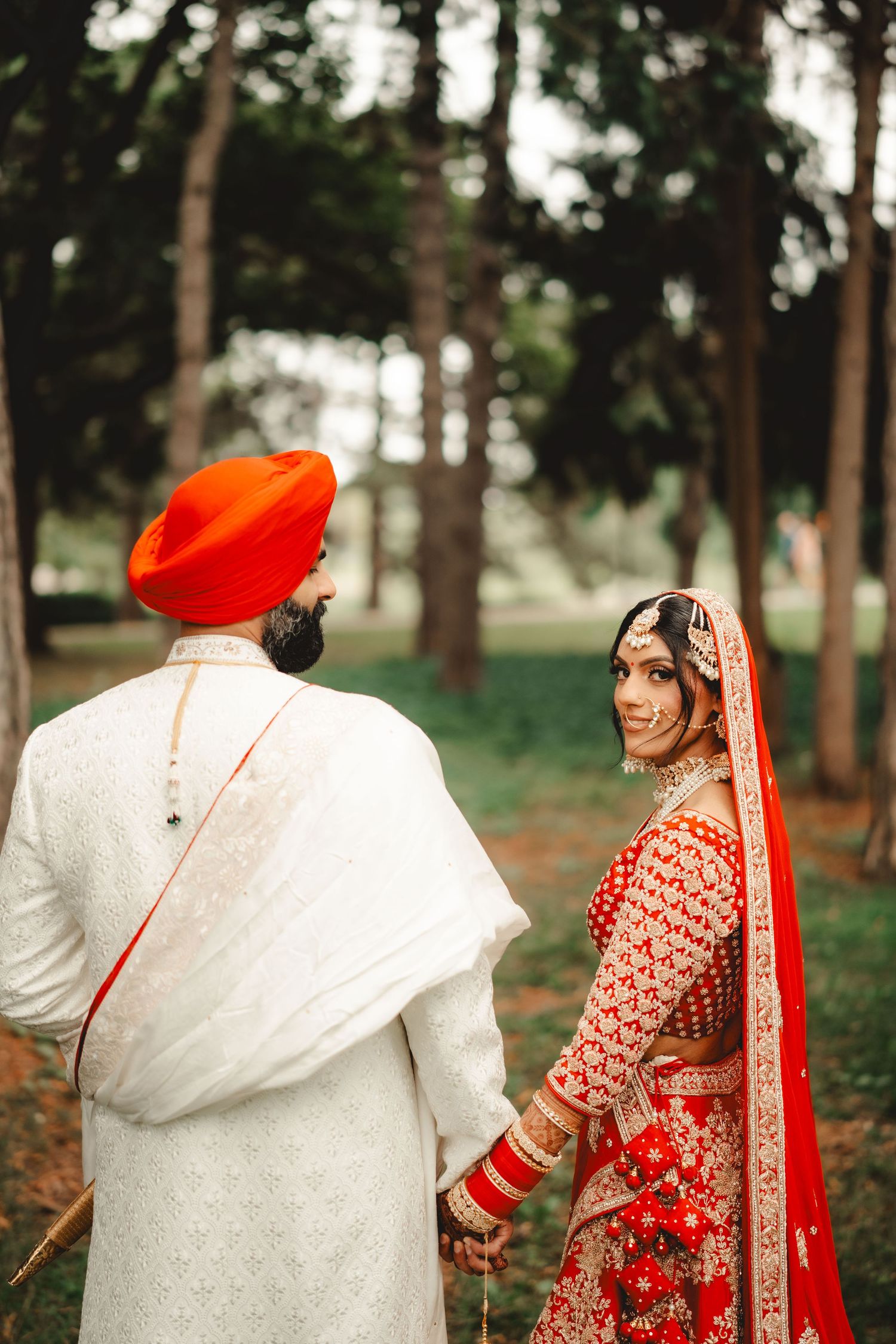 Wedding couple in traditional Sikh attire walking through a wooded park.
