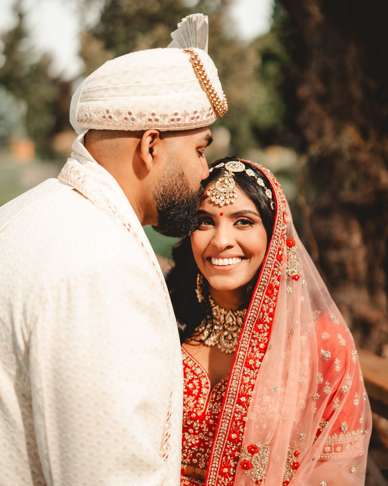 A close-up of a couple in Indian wedding attire sharing a tender moment outdoors.