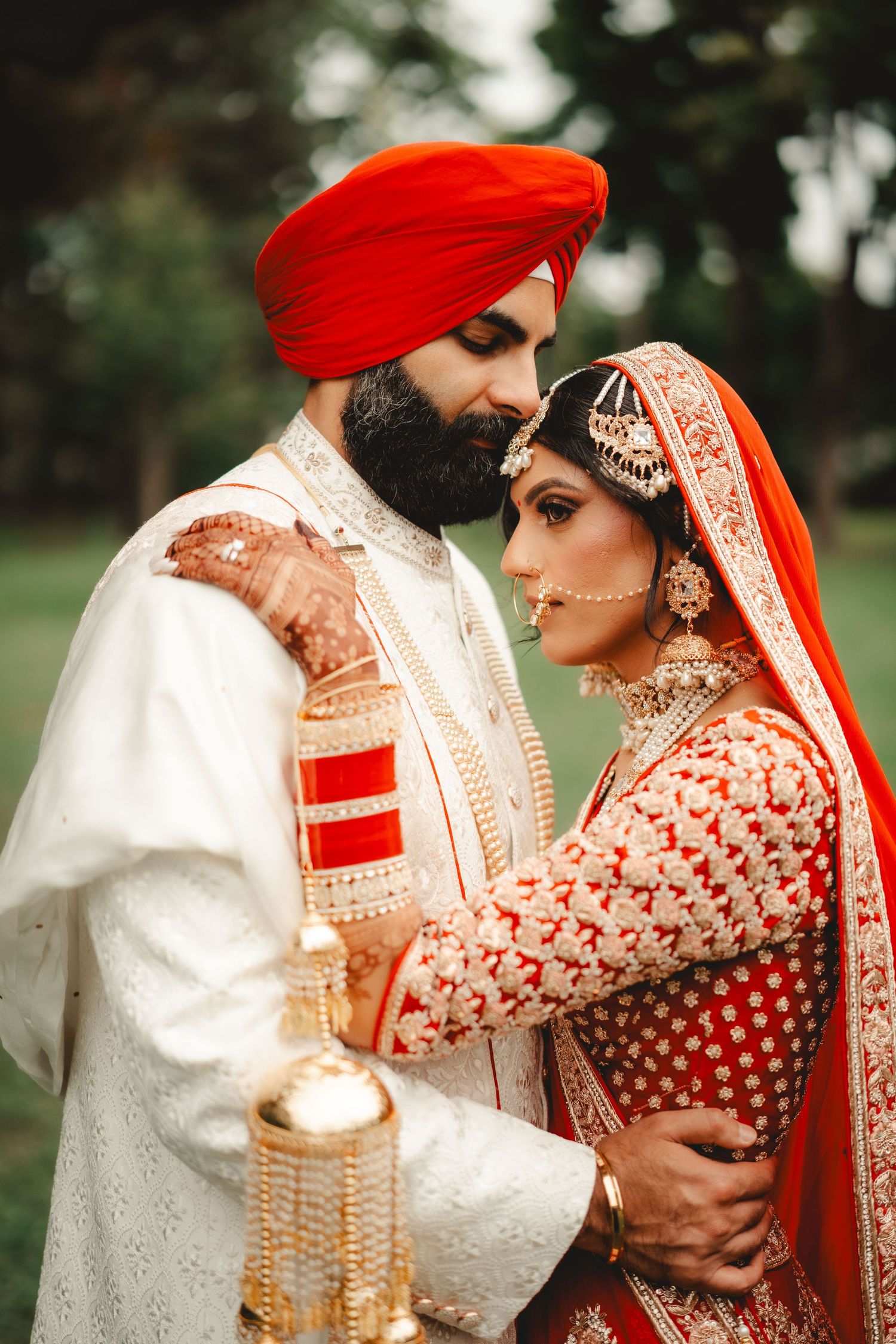 Traditional Sikh wedding couple in red and white attire sharing an intimate moment.