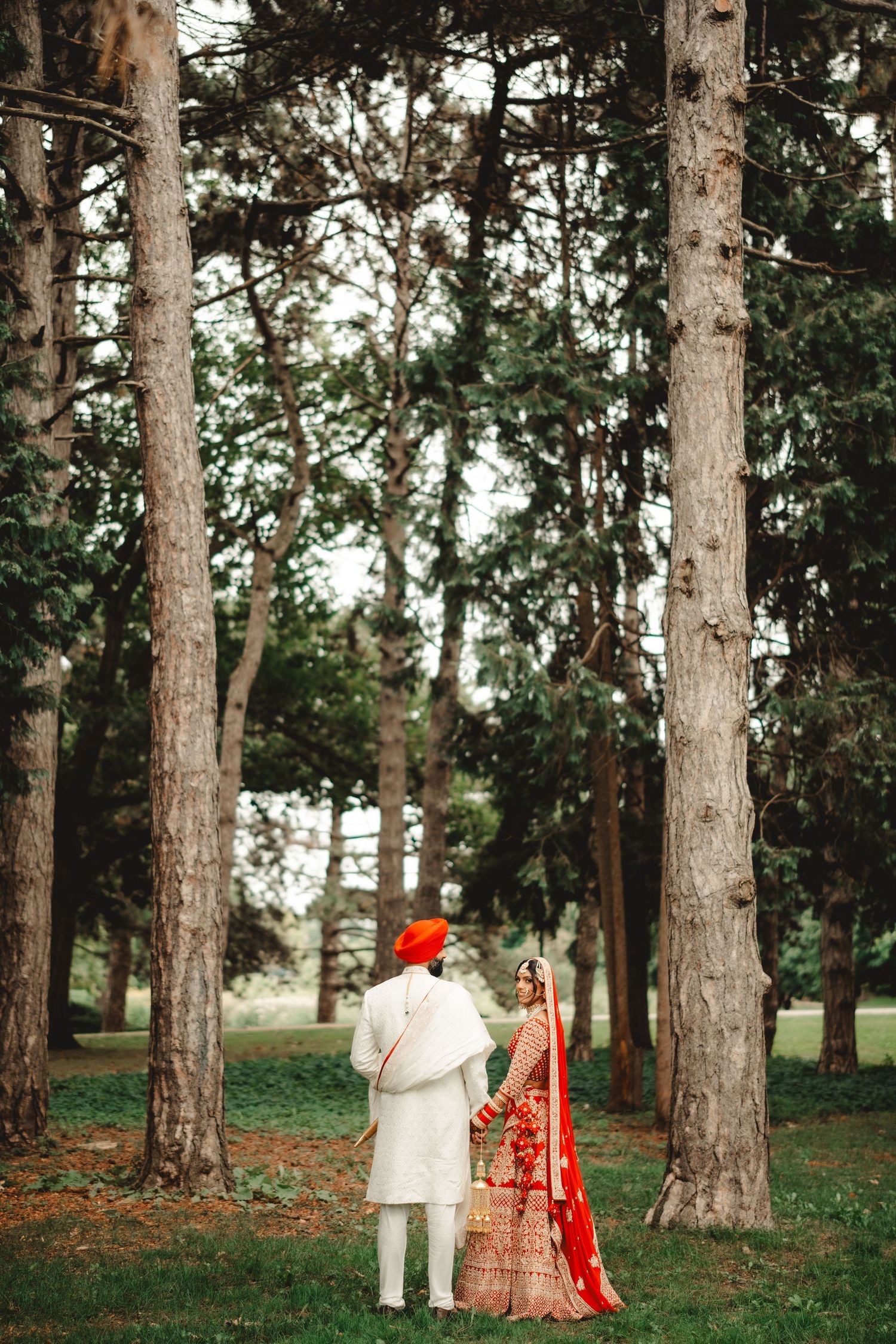 Couple in traditional Indian wedding attire photographed between tall pine trees.