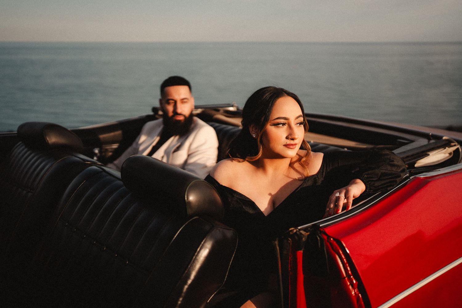 A couple relaxes in a vintage convertible car by the ocean at sunset.