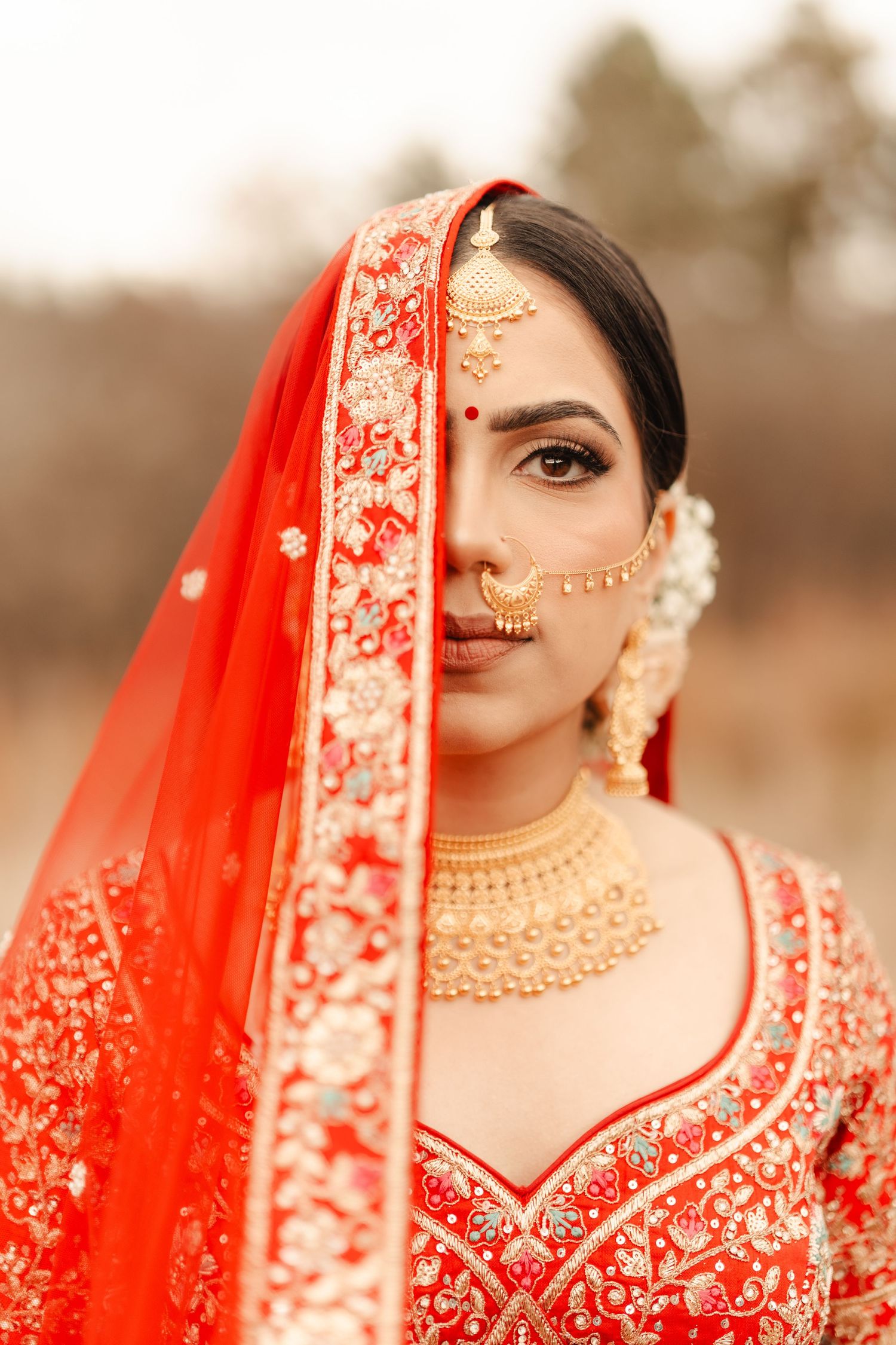 Traditional Indian bridal attire featuring an ornate red dupatta with gold embroidery and intricate jewelry details.