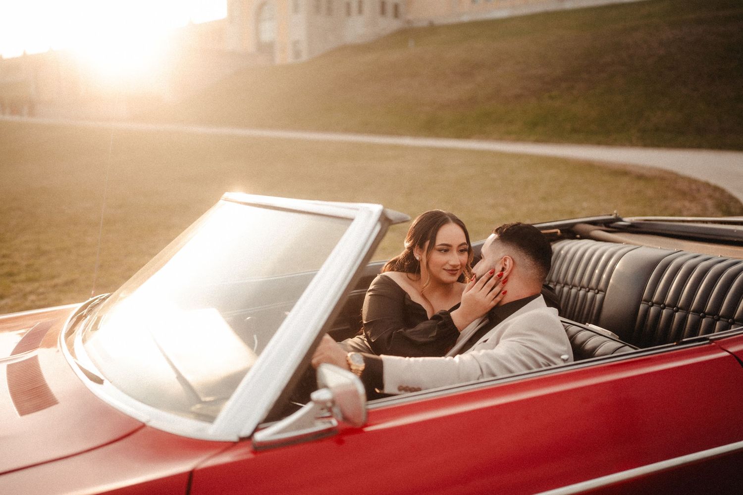 A couple shares a romantic moment while sitting in a vintage red convertible car at sunset.