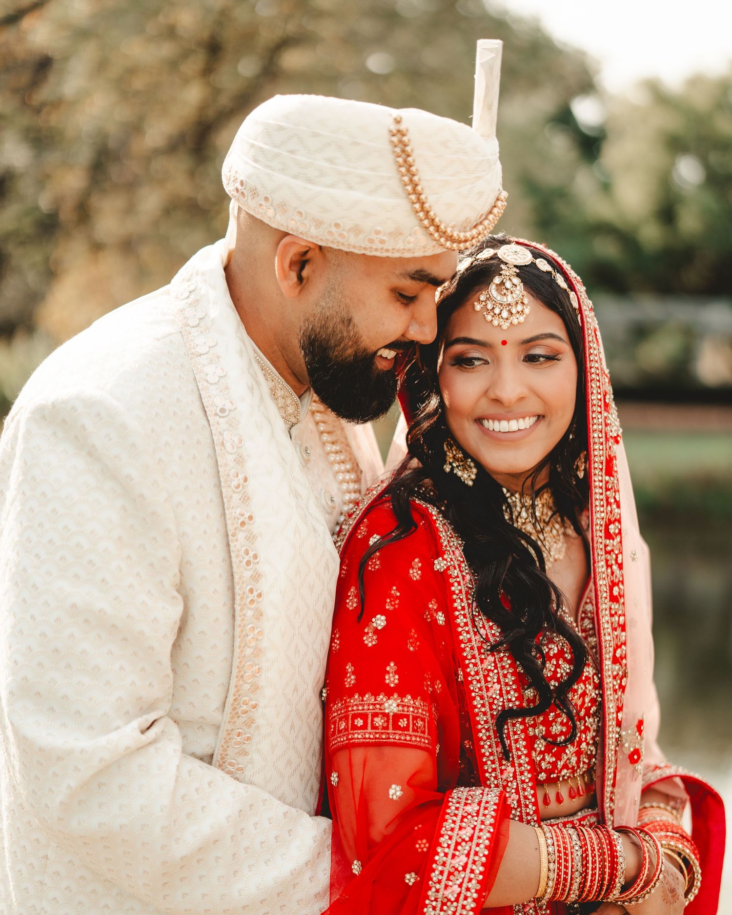 A couple shares an intimate moment wearing traditional Indian wedding outfits in an outdoor setting.
