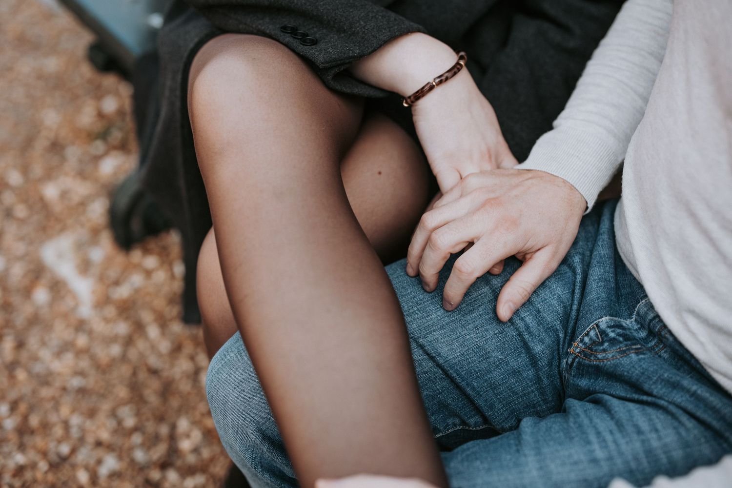 Casual couple sitting together on rustic ground during outdoor photo session.