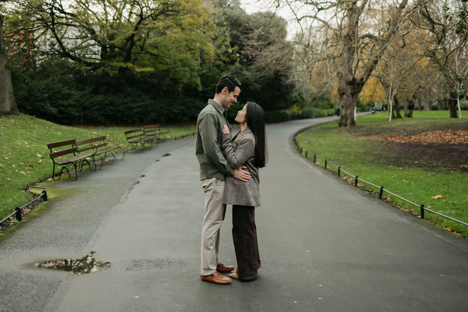 Couple sharing a romantic moment on a winding park path surrounded by autumn trees.