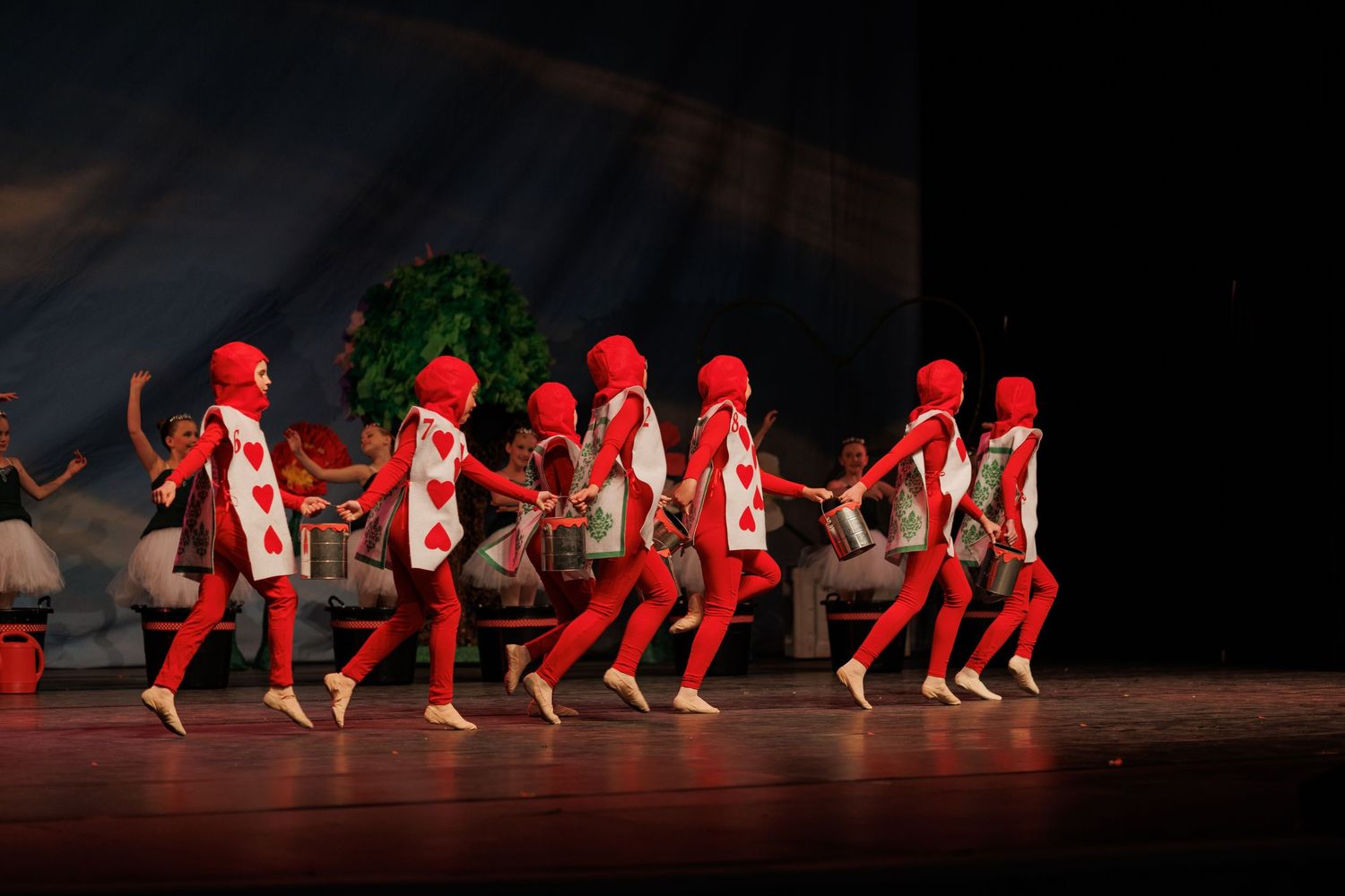Dancers in bright red costumes perform a synchronized choreographed dance routine on a dark stage.
