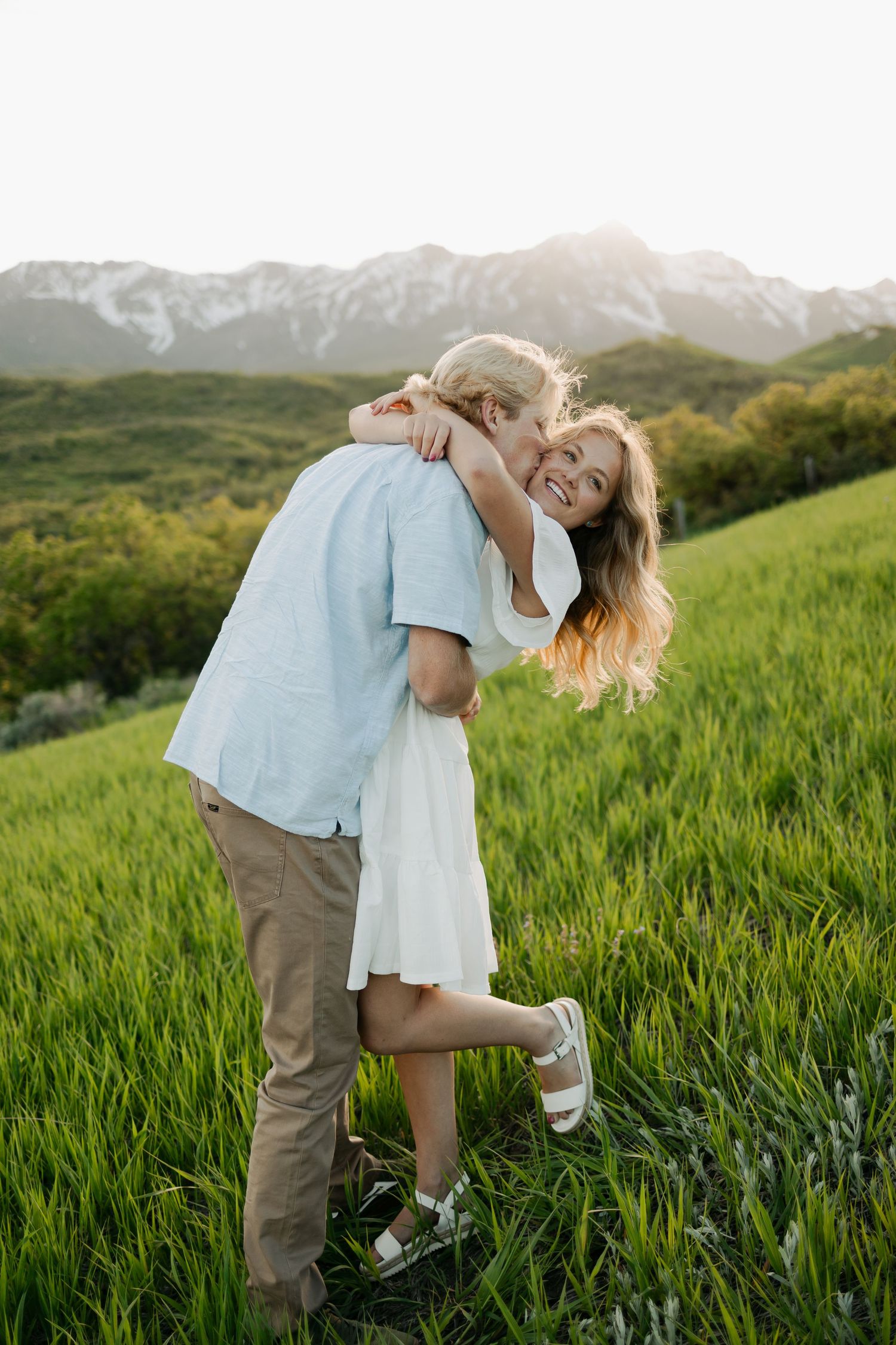Romantic couple playing and embracing in green field during sunset.