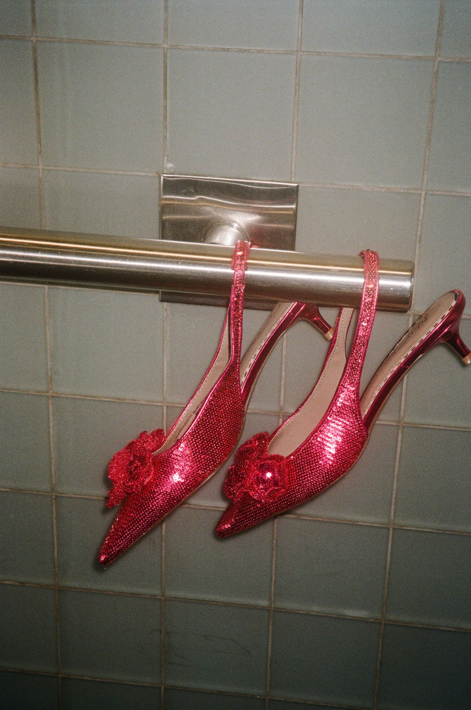A pair of sparkly red slingback heels with decorative pom poms hanging on a bathroom towel bar.