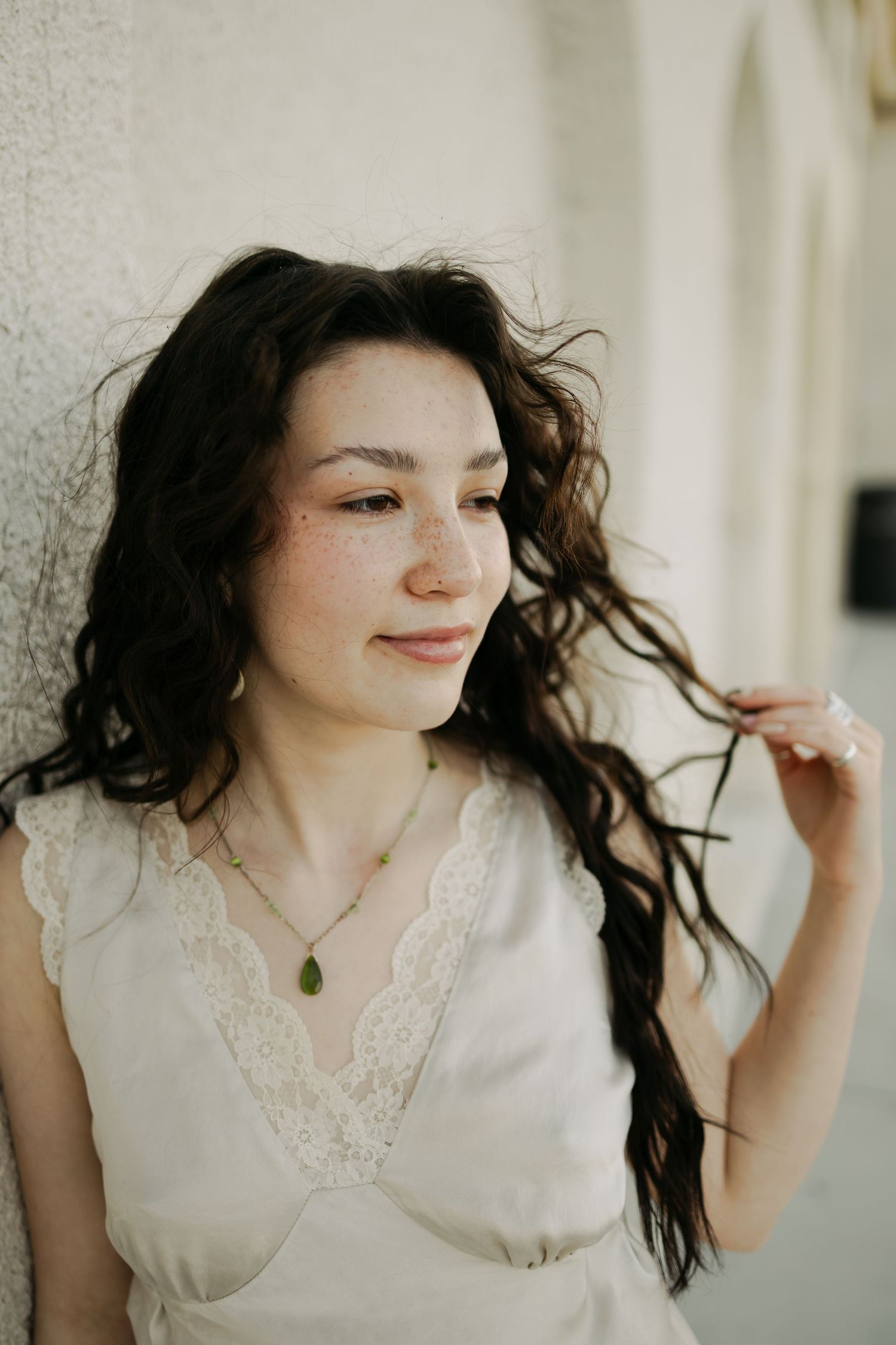 Woman in white lace top playfully tosses her dark curly hair against a light background.