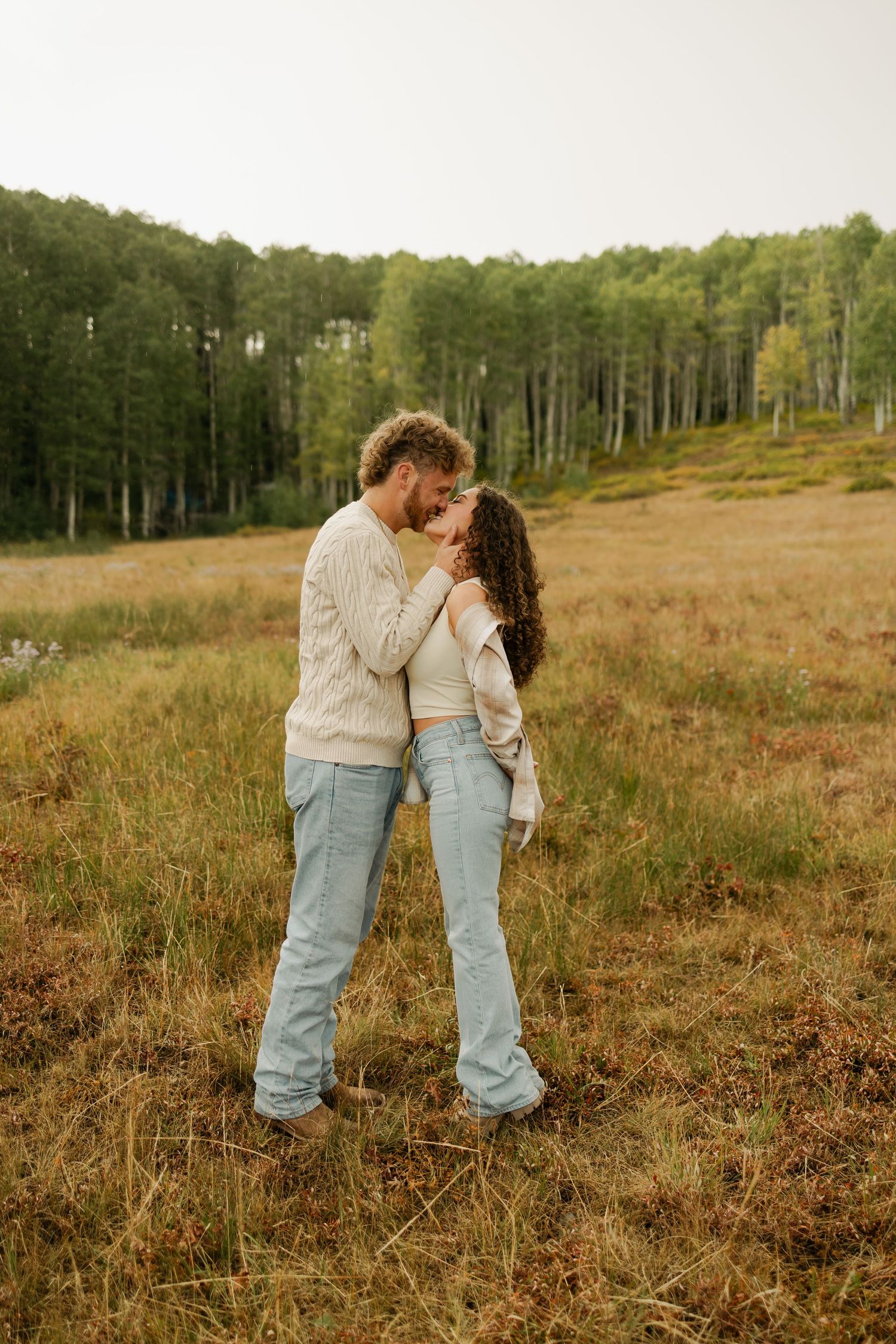 A couple in casual denim outfits shares intimate moments in a scenic field.