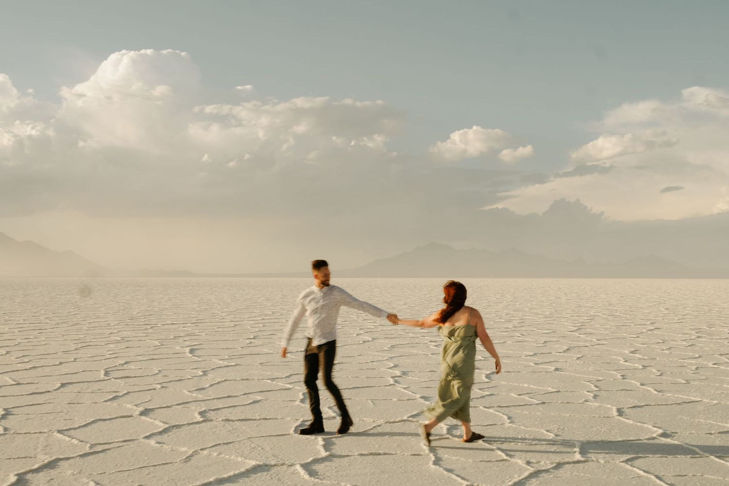 Couple dancing together on salt flats during sunset with mountains in background.
