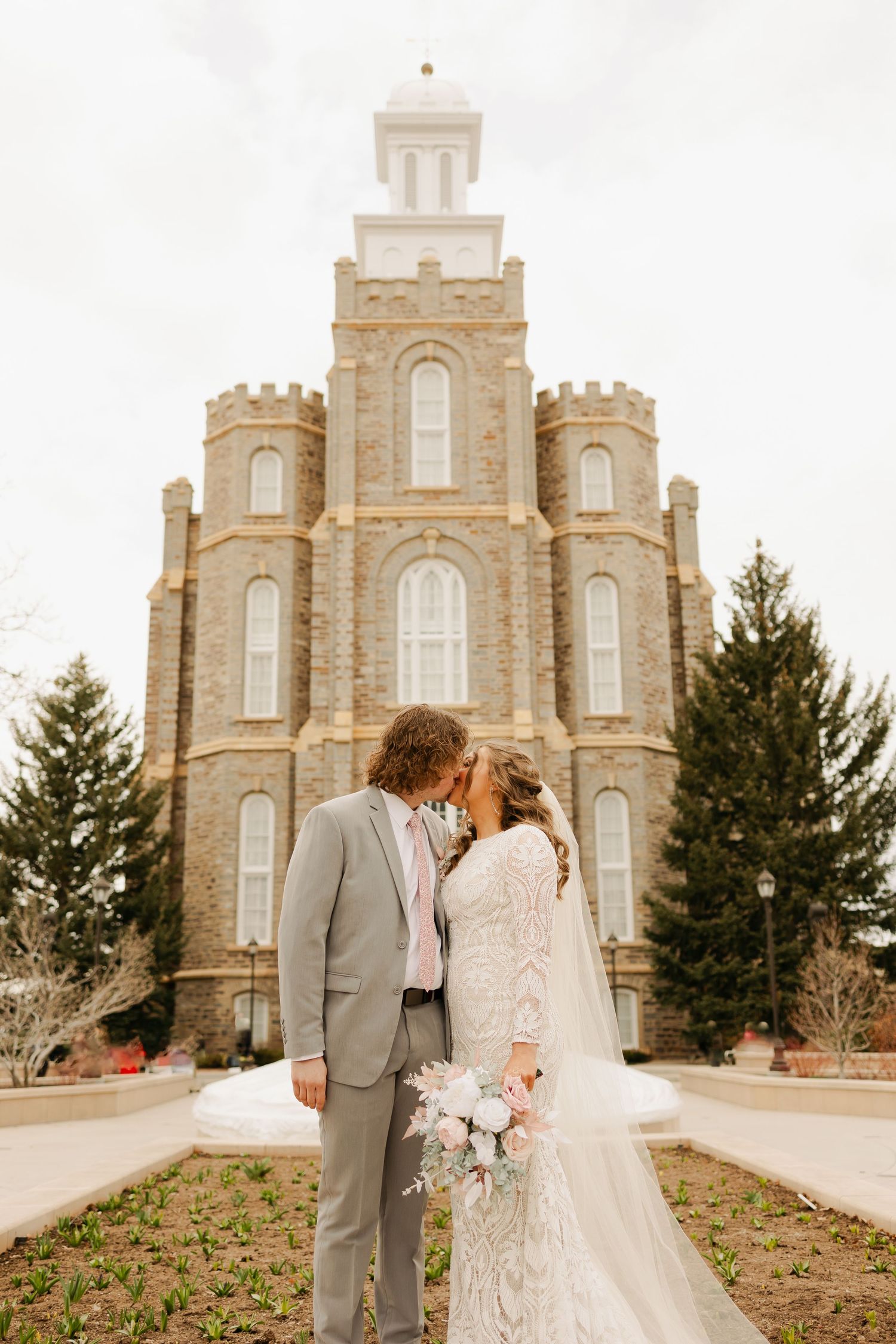 A wedding couple poses in front of a grand stone temple with elegant architecture and spires.