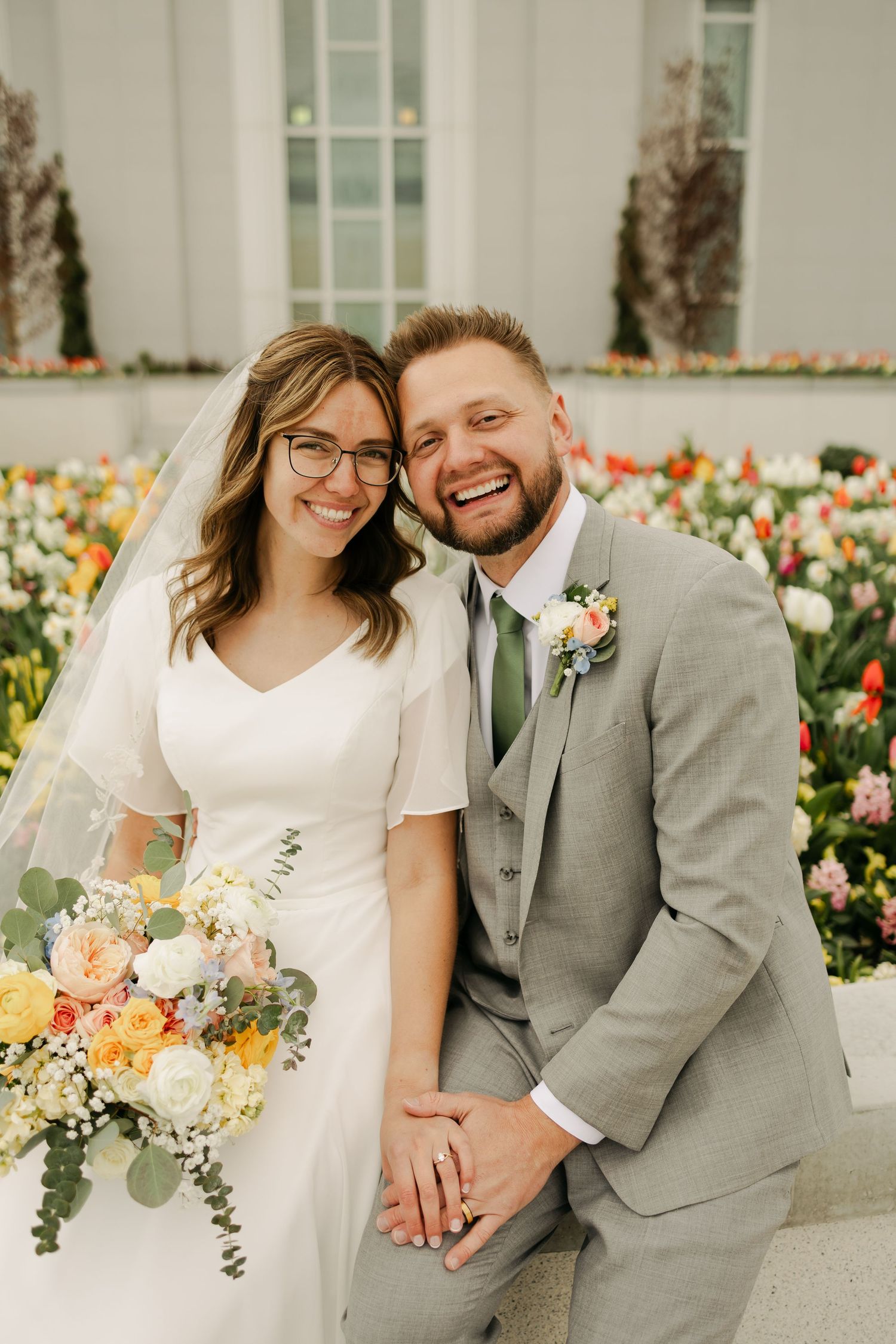Wedding couple sitting among spring tulips in formal attire.