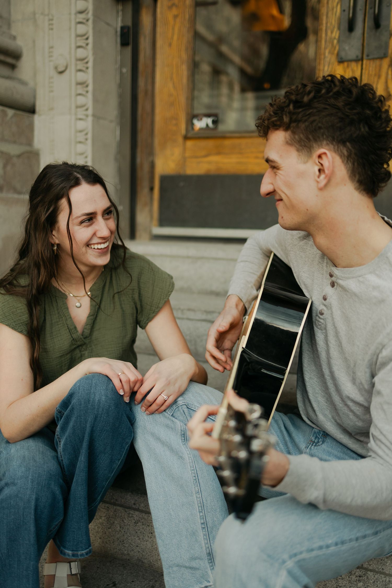 Two people share laughs while playing acoustic guitar together indoors.