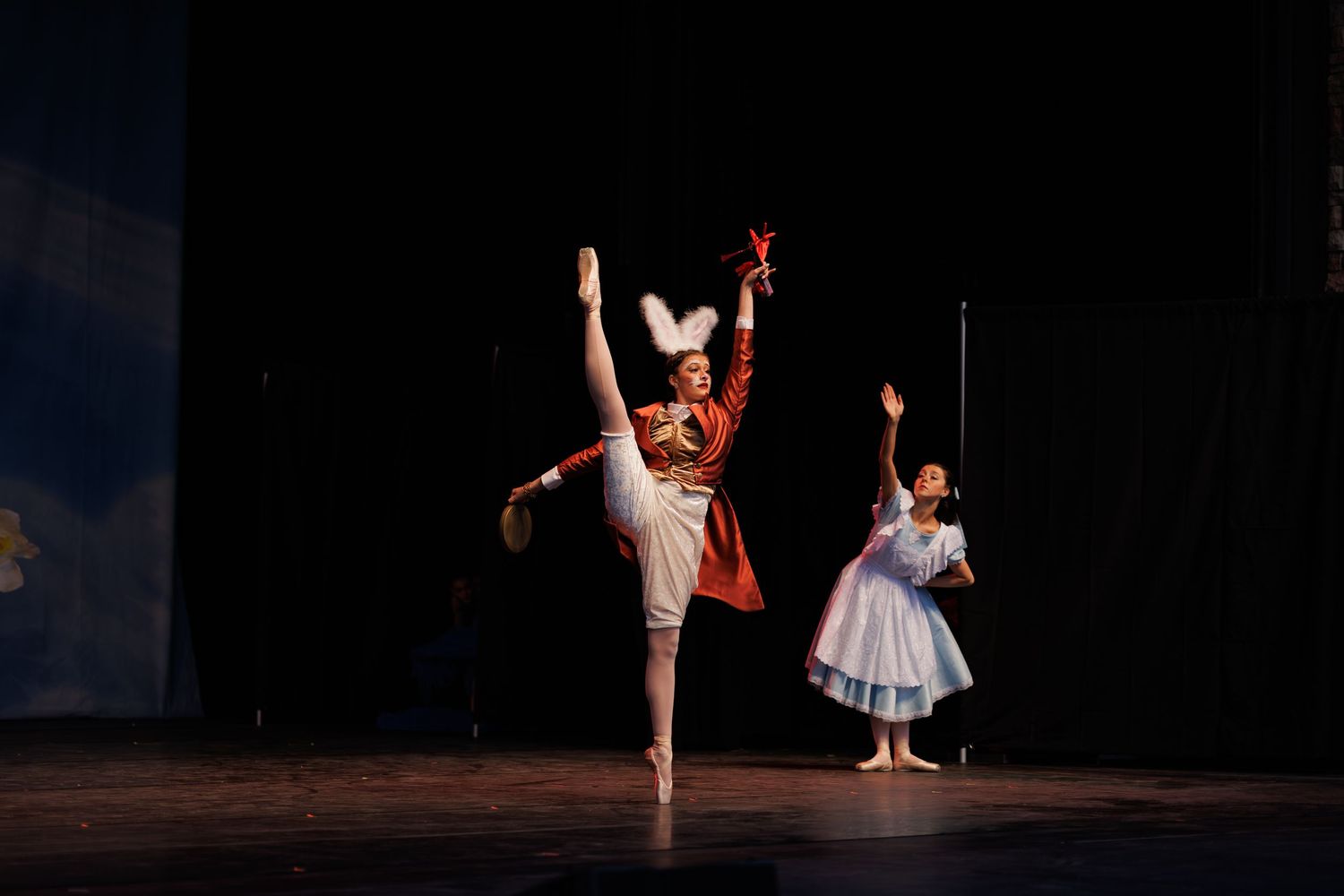 A ballet dancer performs gracefully in a white tutu on a dark stage during a classical performance.