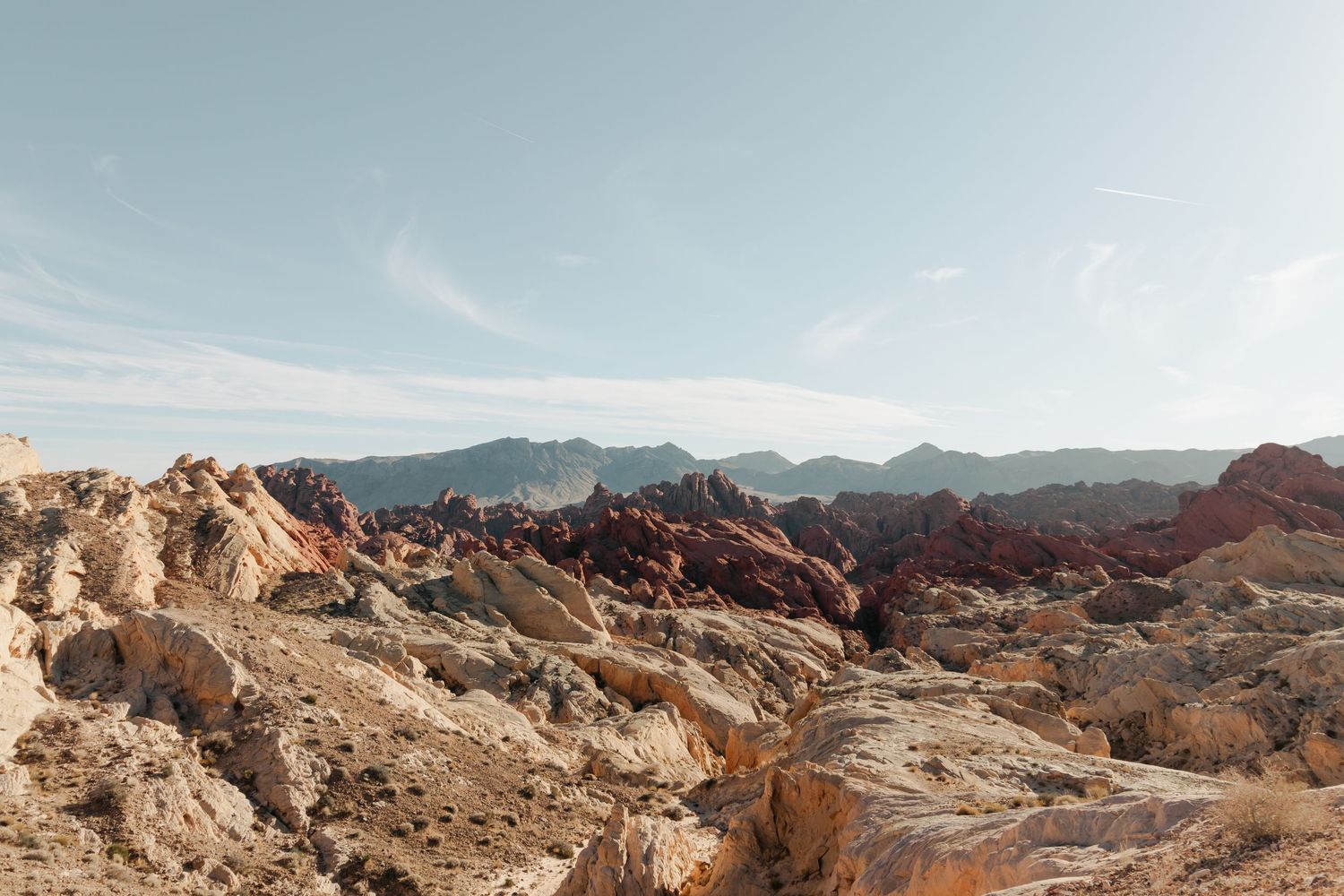 Rugged desert landscape with colorful red and orange rock formations under a pale blue sky.