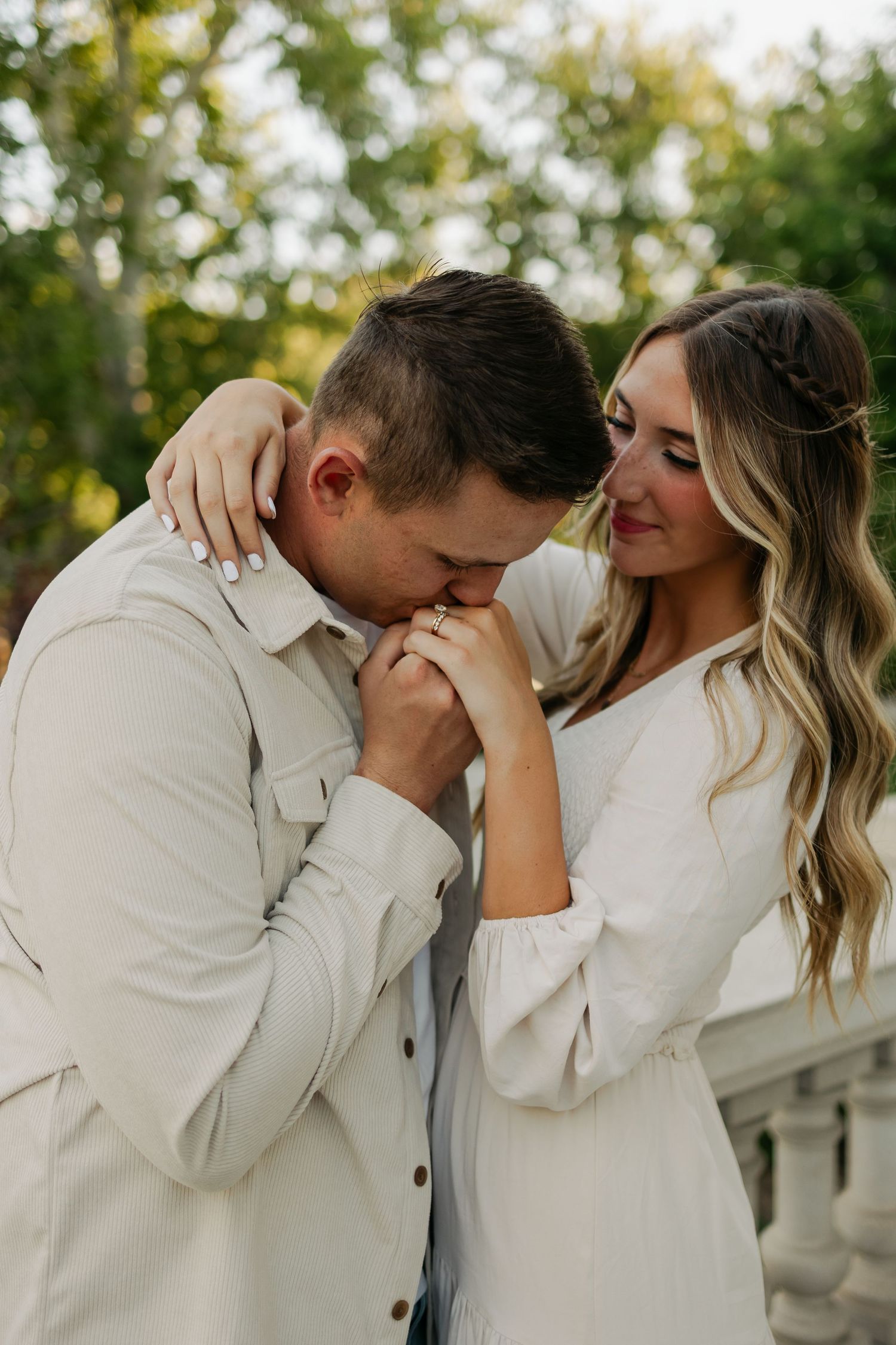 Couple in matching white outfits share tender romantic moments outdoors during photo session.