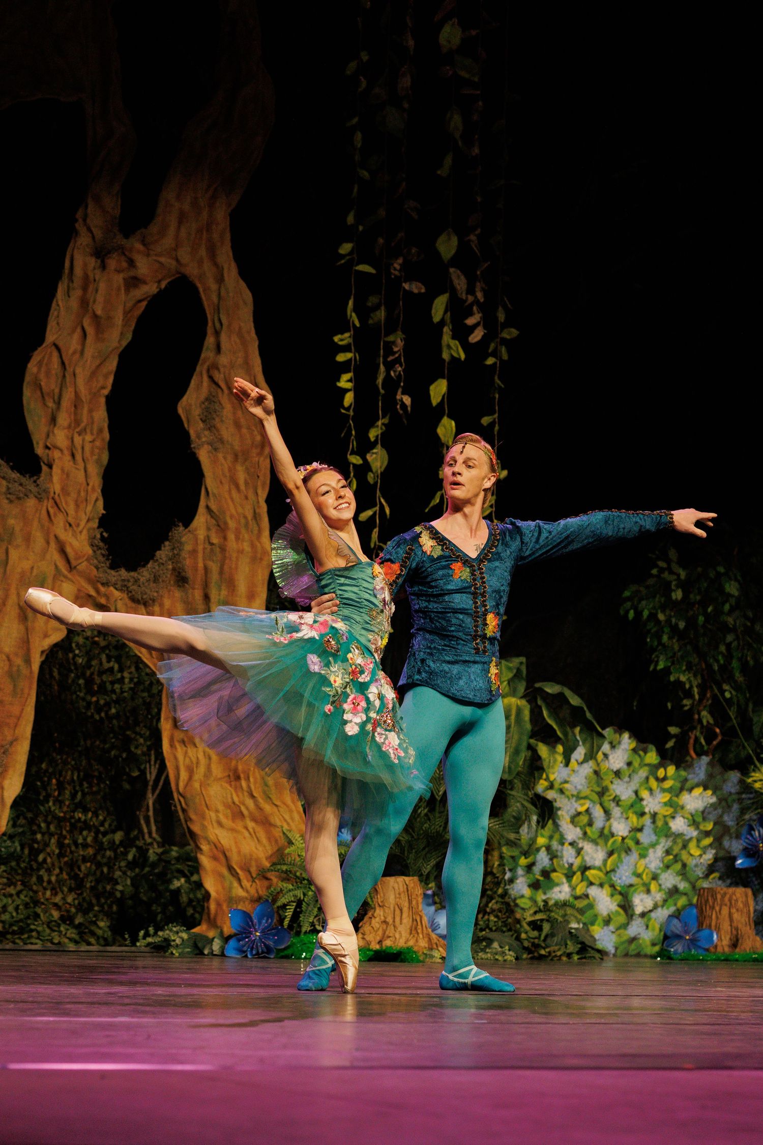 Ballet dancers perform an elegant pas de deux on stage with theatrical scenery and dramatic lighting.