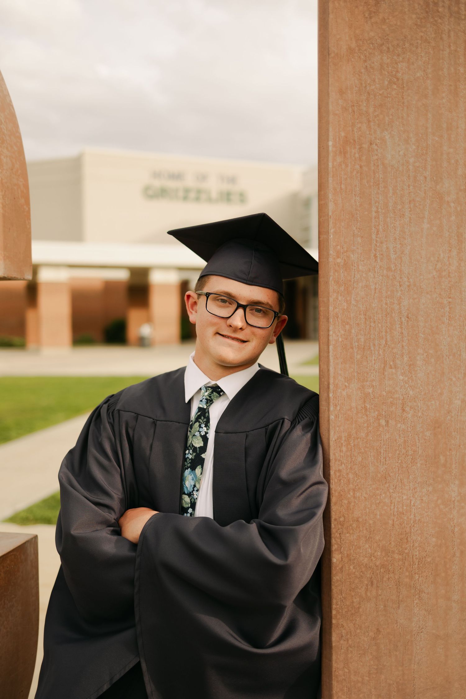 Graduate in cap and gown posing confidently against a column at their university.