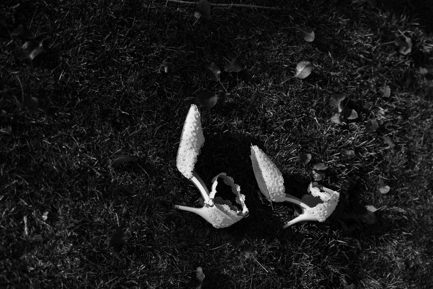 Black and white artistic photo of wedding shoes on a dark textured surface.