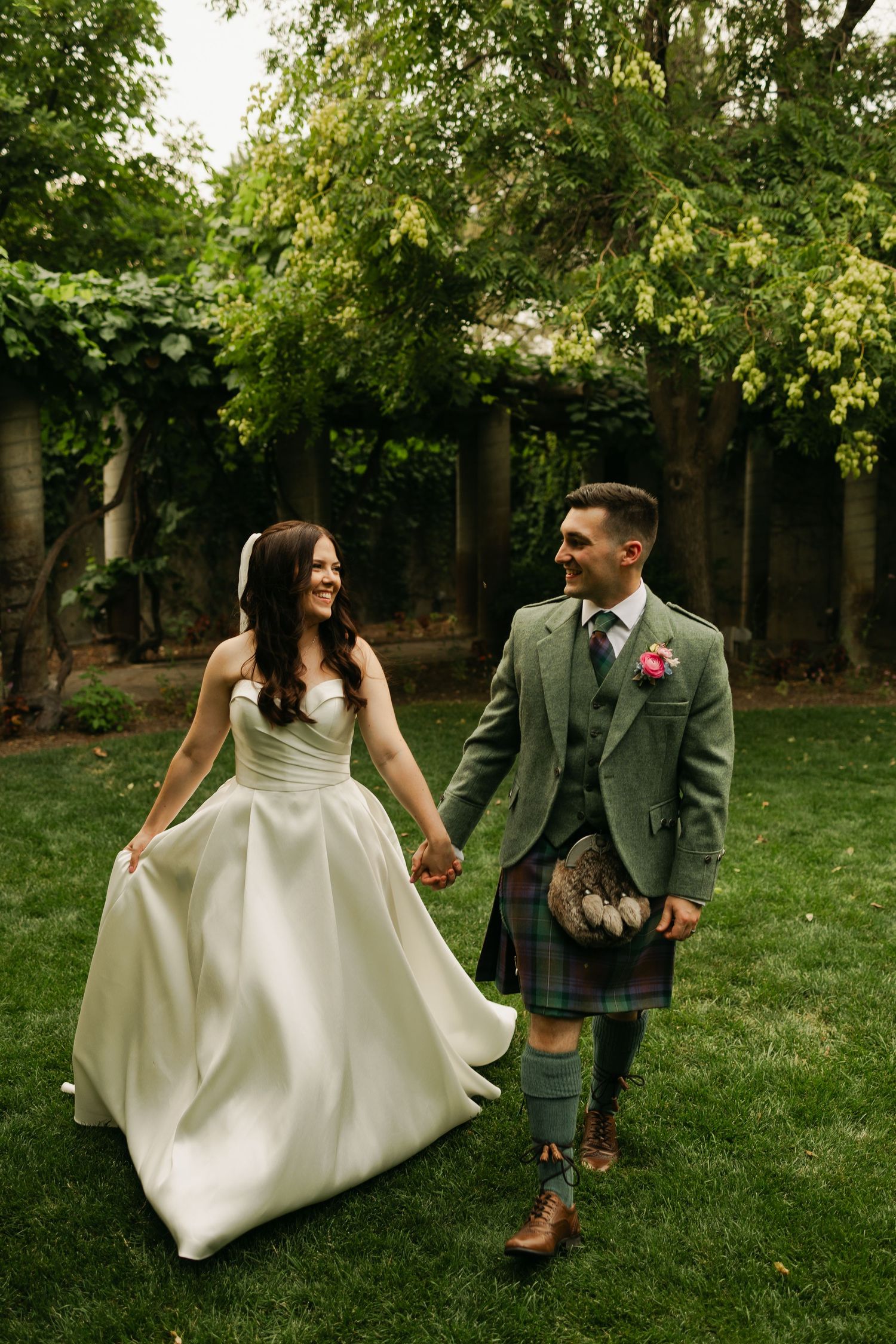 Newlyweds walking hand in hand with groom wearing traditional Scottish kilt.