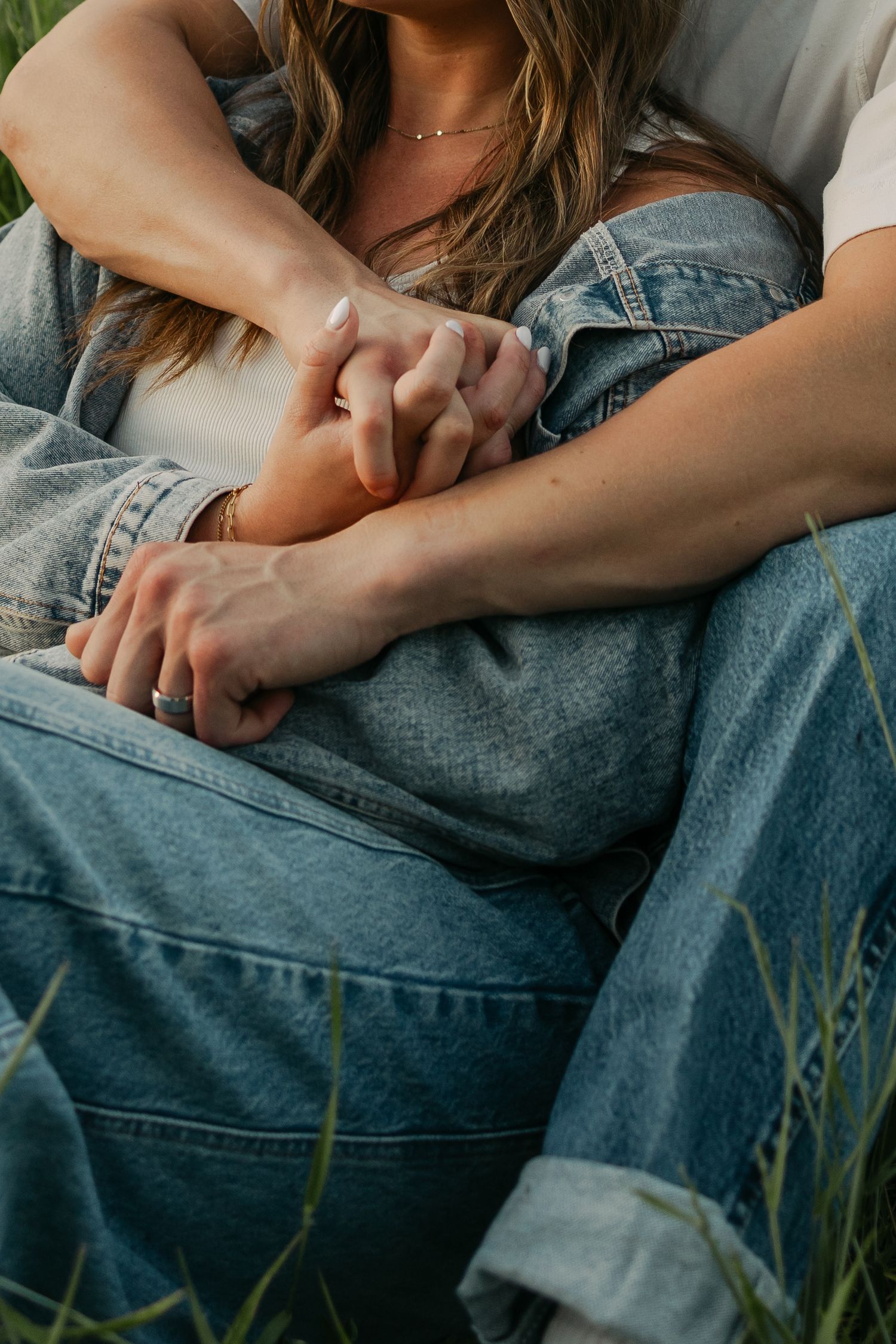 Close-up shot of hands resting on denim jeans with grass in the background.