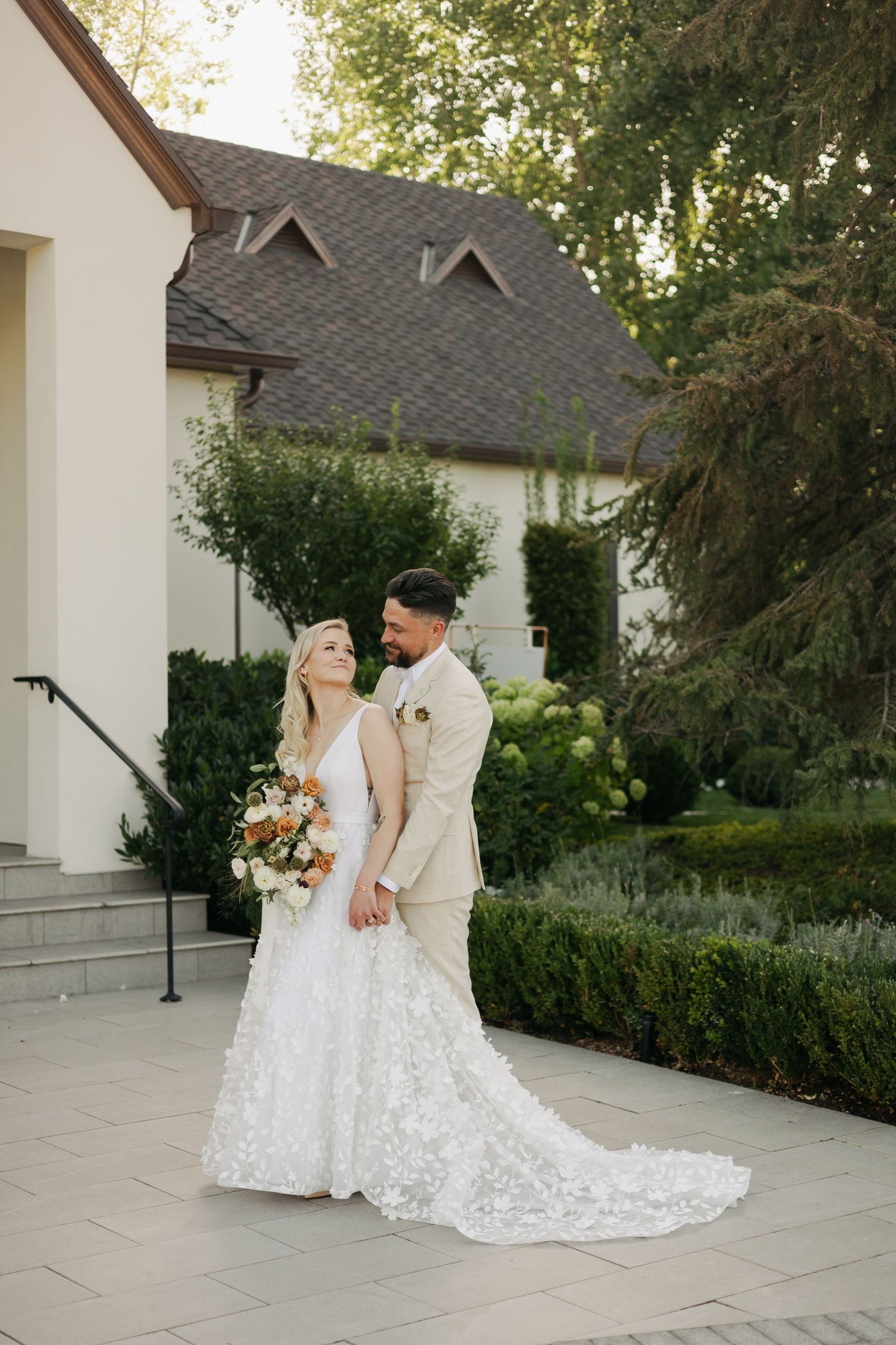Newlyweds sharing romantic moment outside white chapel with lush garden.