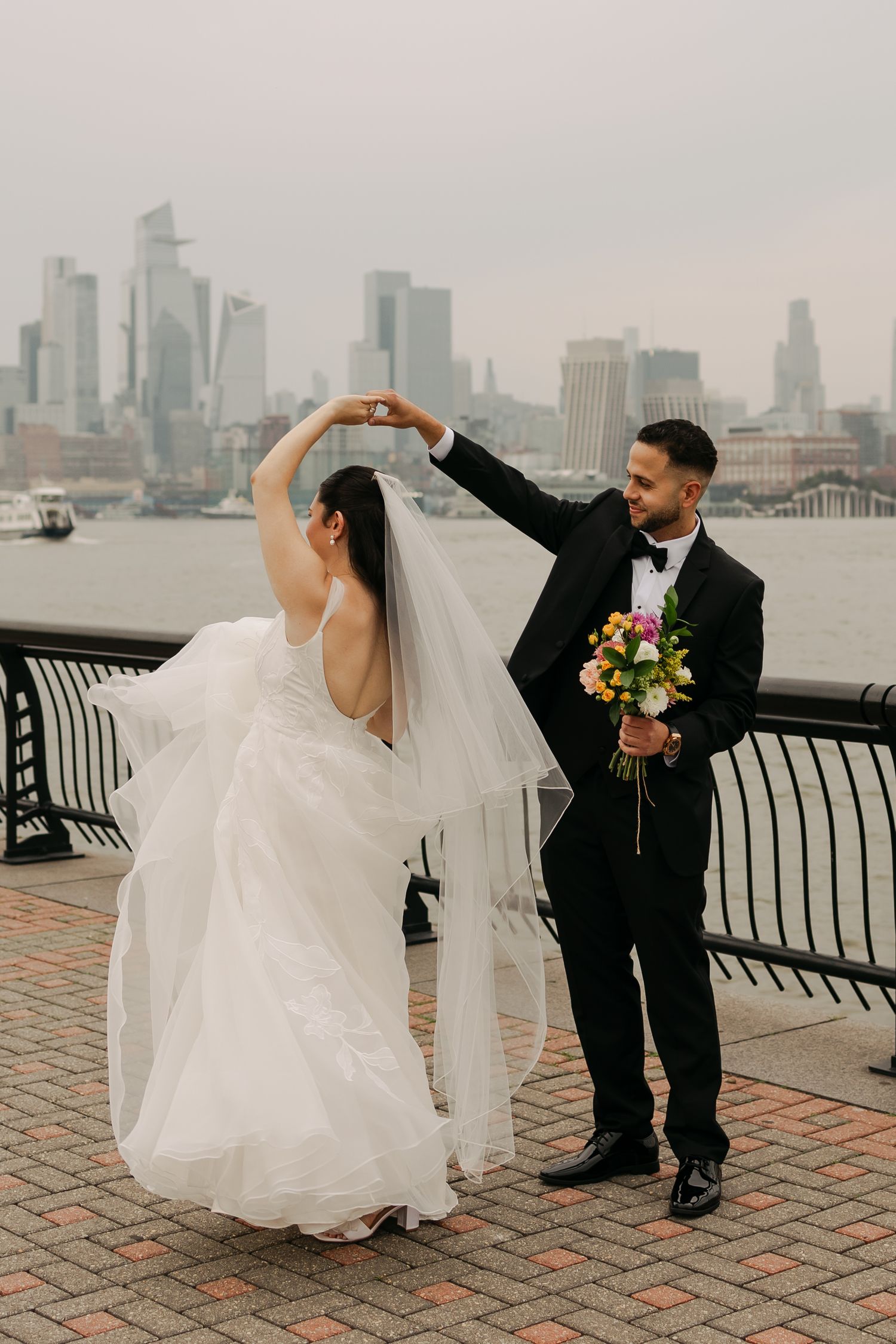Couple dancing on brick promenade with urban skyline backdrop during wedding photoshoot.