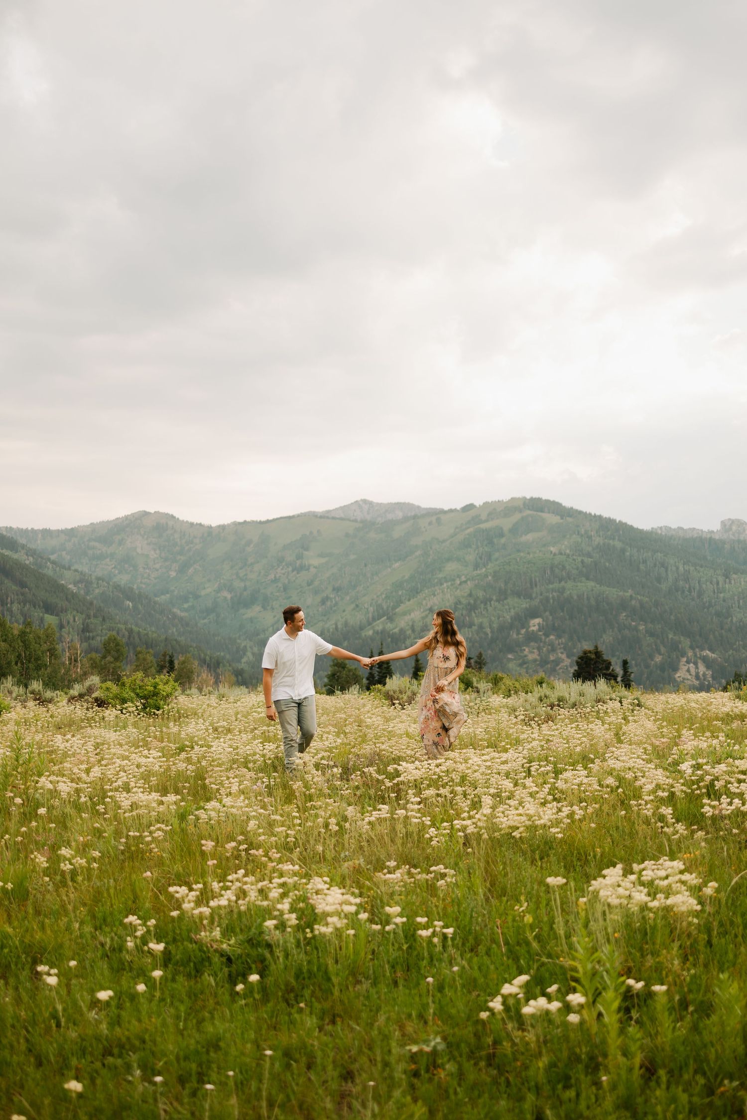 Couple running through mountain wildflower meadow on sunny afternoon.