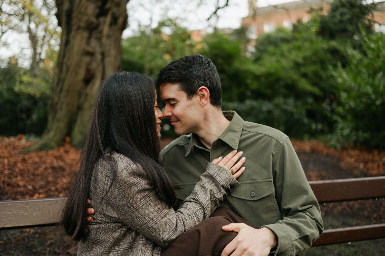 Couple sharing an intimate moment on a park bench surrounded by autumn foliage and trees.