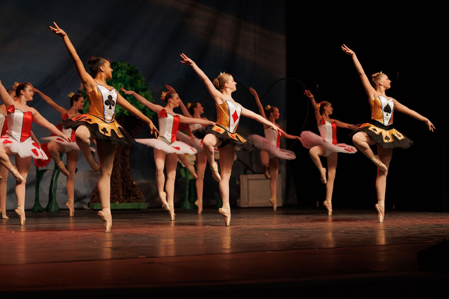 Ballet dancers in white tutus perform synchronized movements together with pointed arms in a classical stage production.